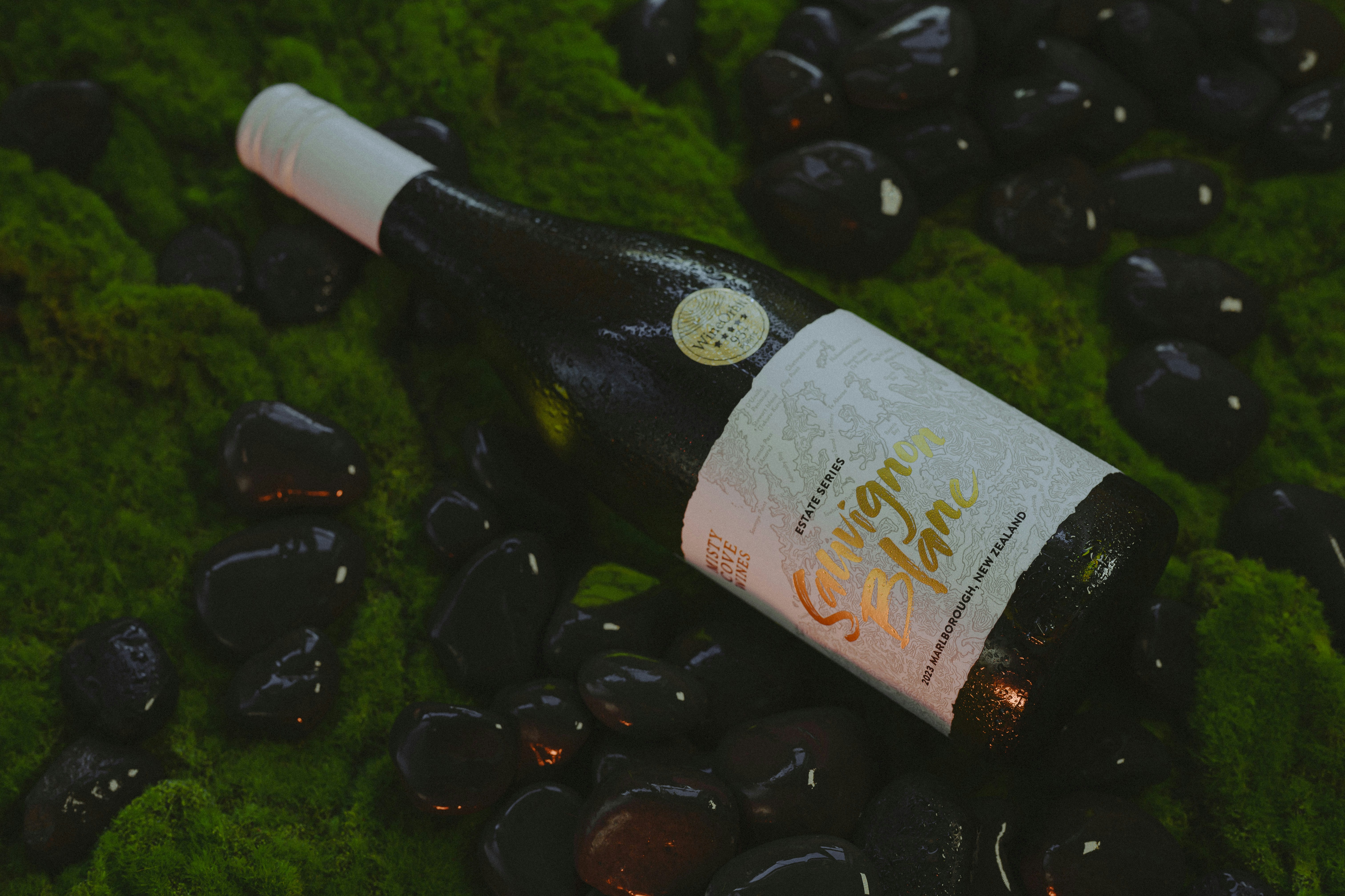 Wine bottle surrounded by black stones and greenery.