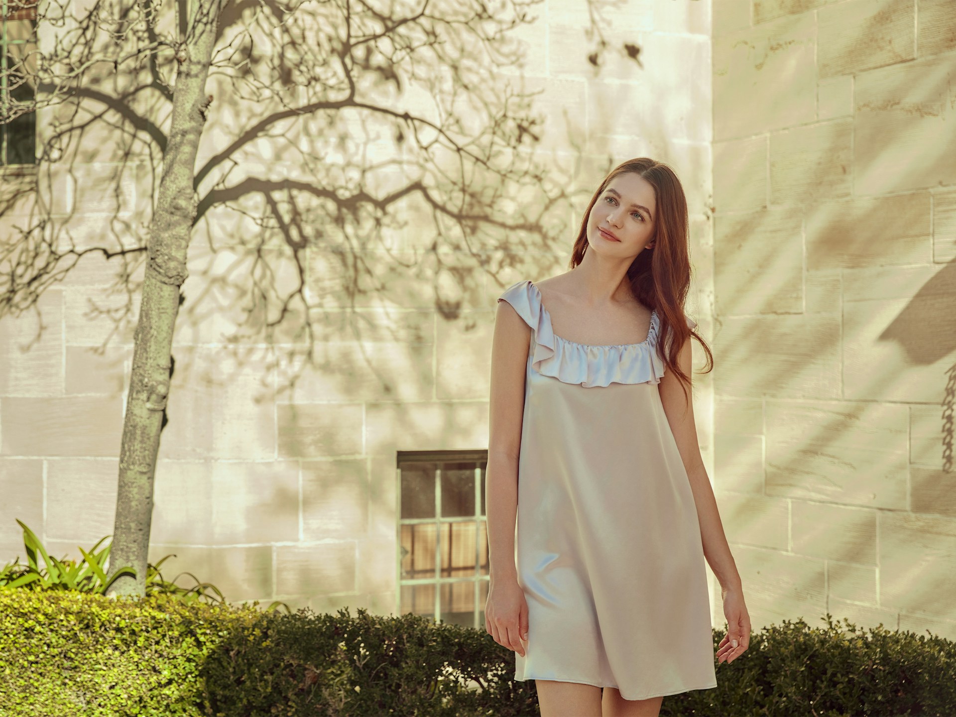 Young woman stands outside near a tree.