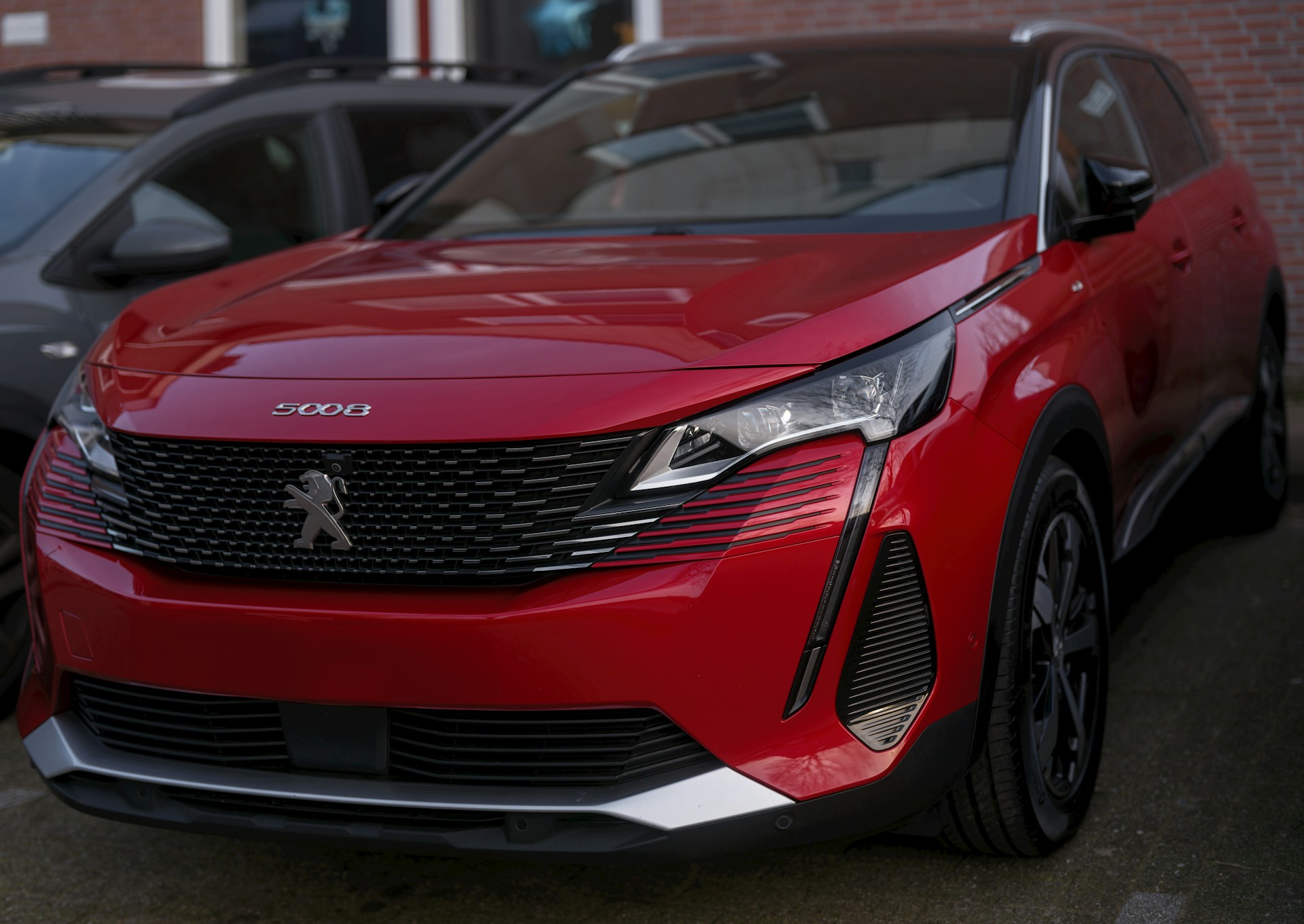 A red peugeot suv is parked outside.