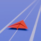 Red paper airplane on a blue track.