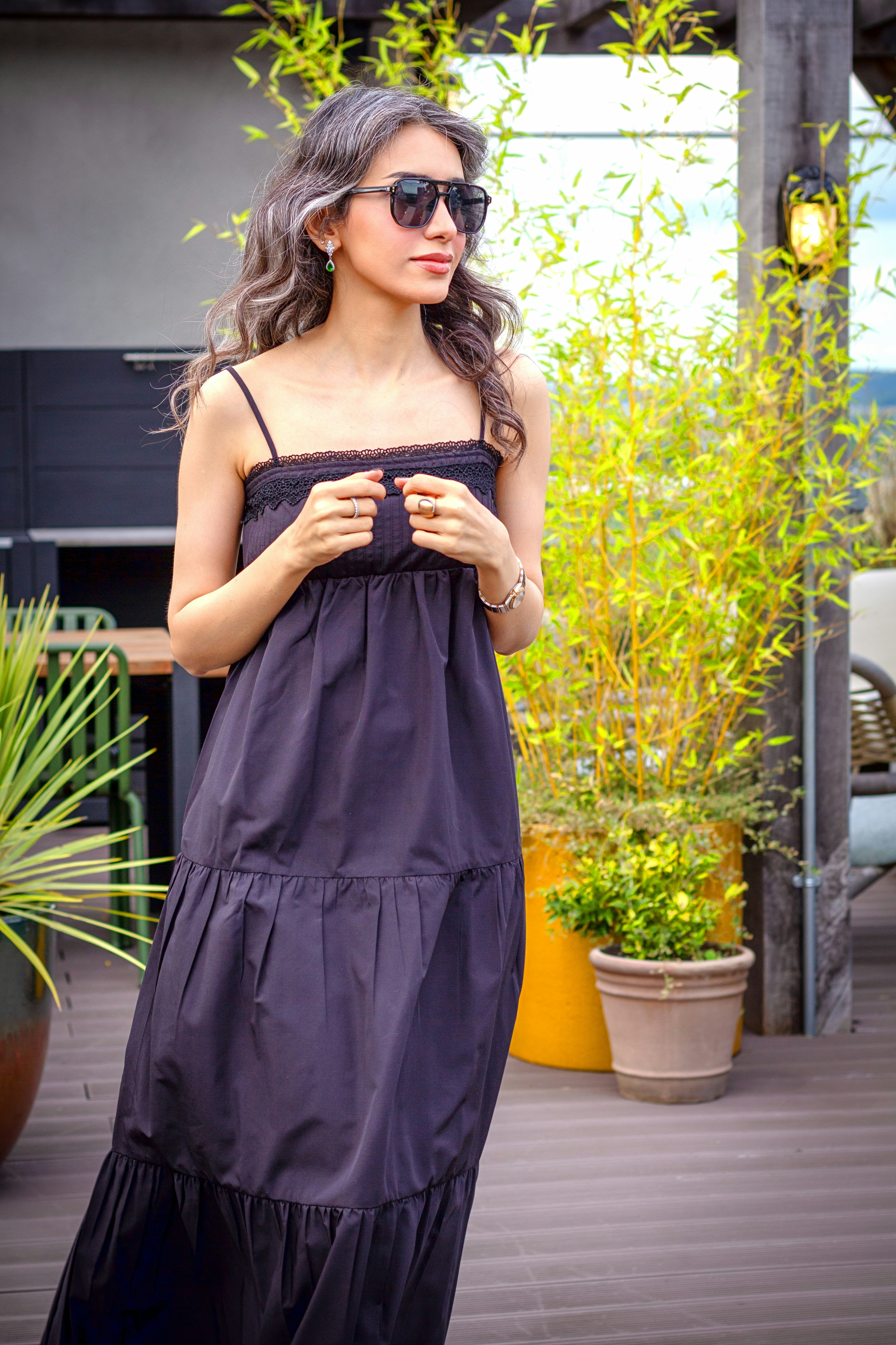 A woman models a black dress and sunglasses outdoors.