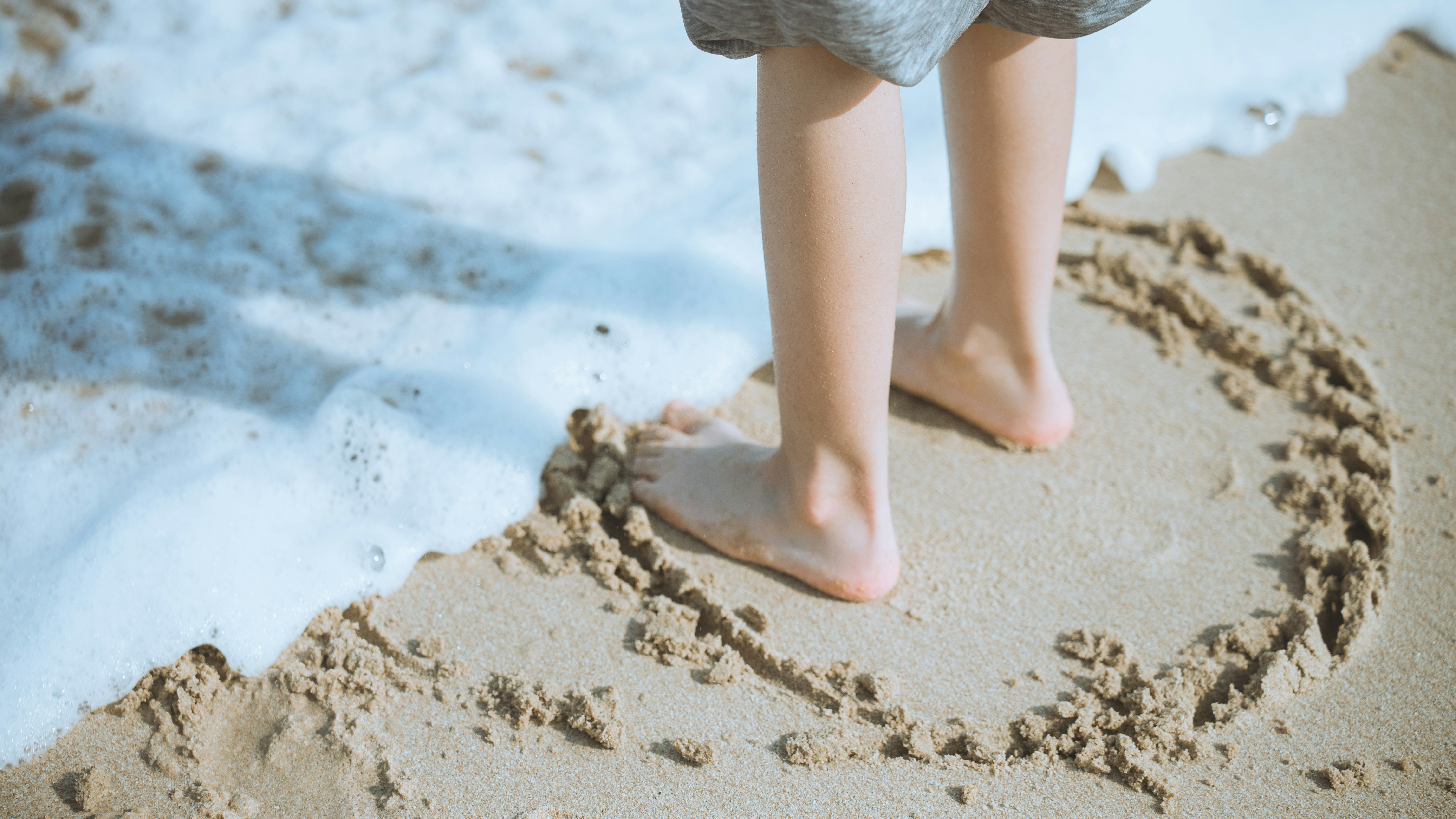 Child's feet in a heart drawn on the sand.