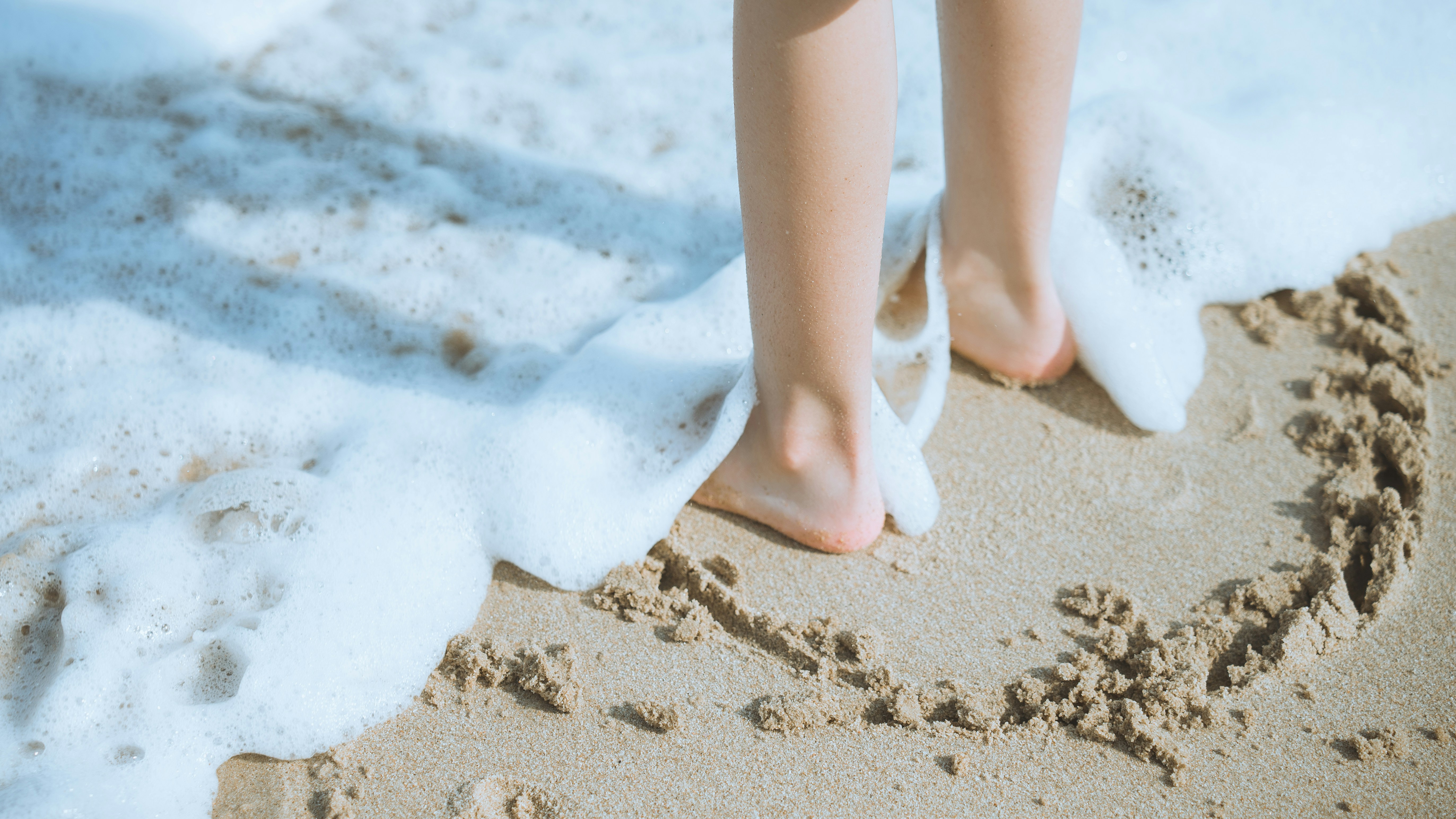 Feet stand in water on the beach.