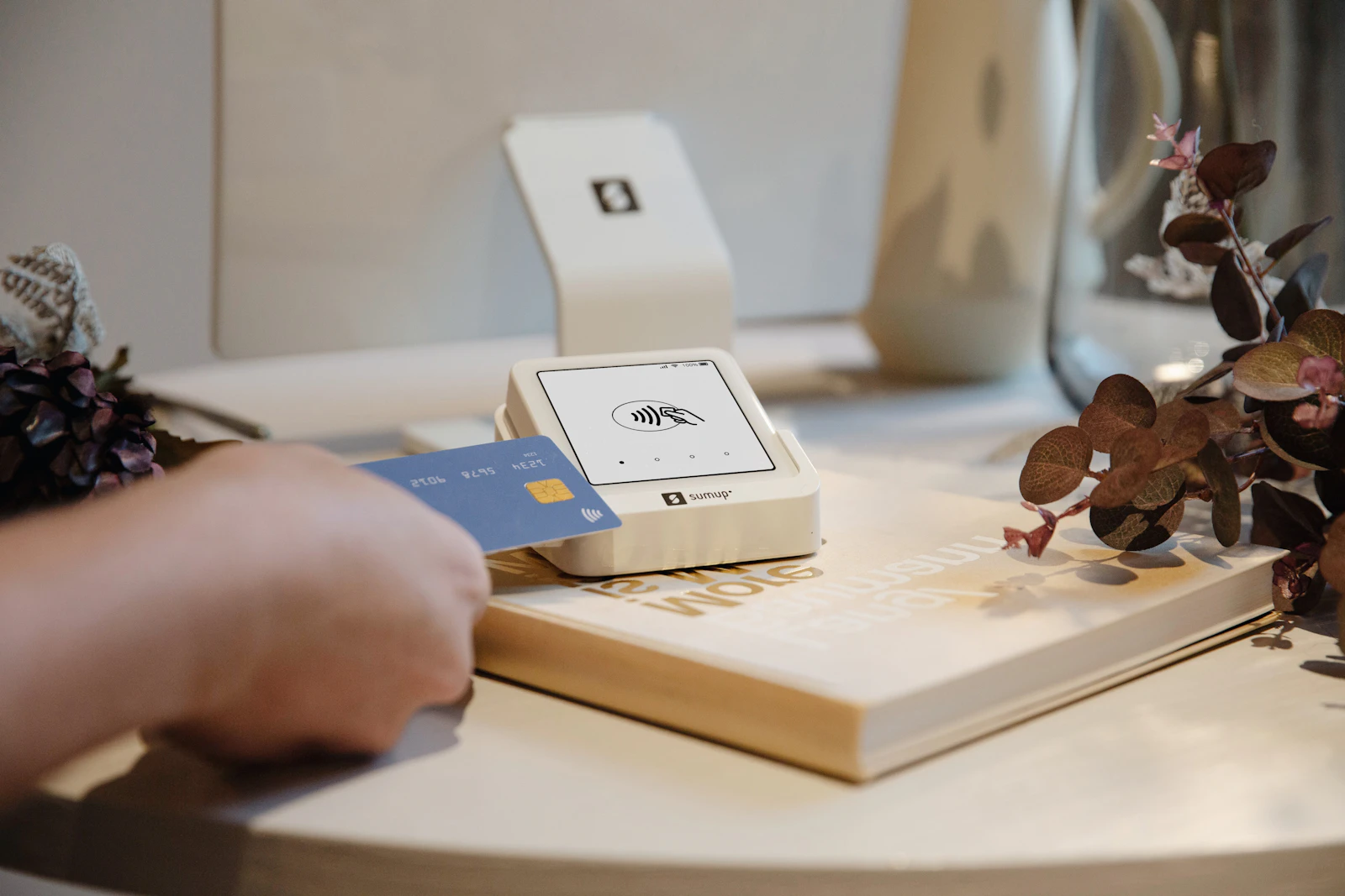 A customer tapping a credit card on a small card reader resting on a book