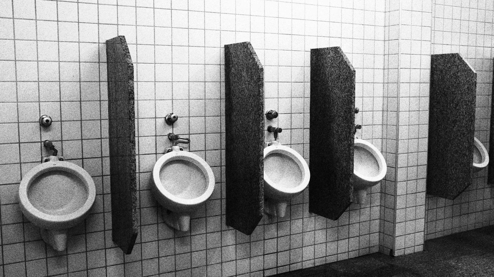Urinals in a bathroom, separated by wood.