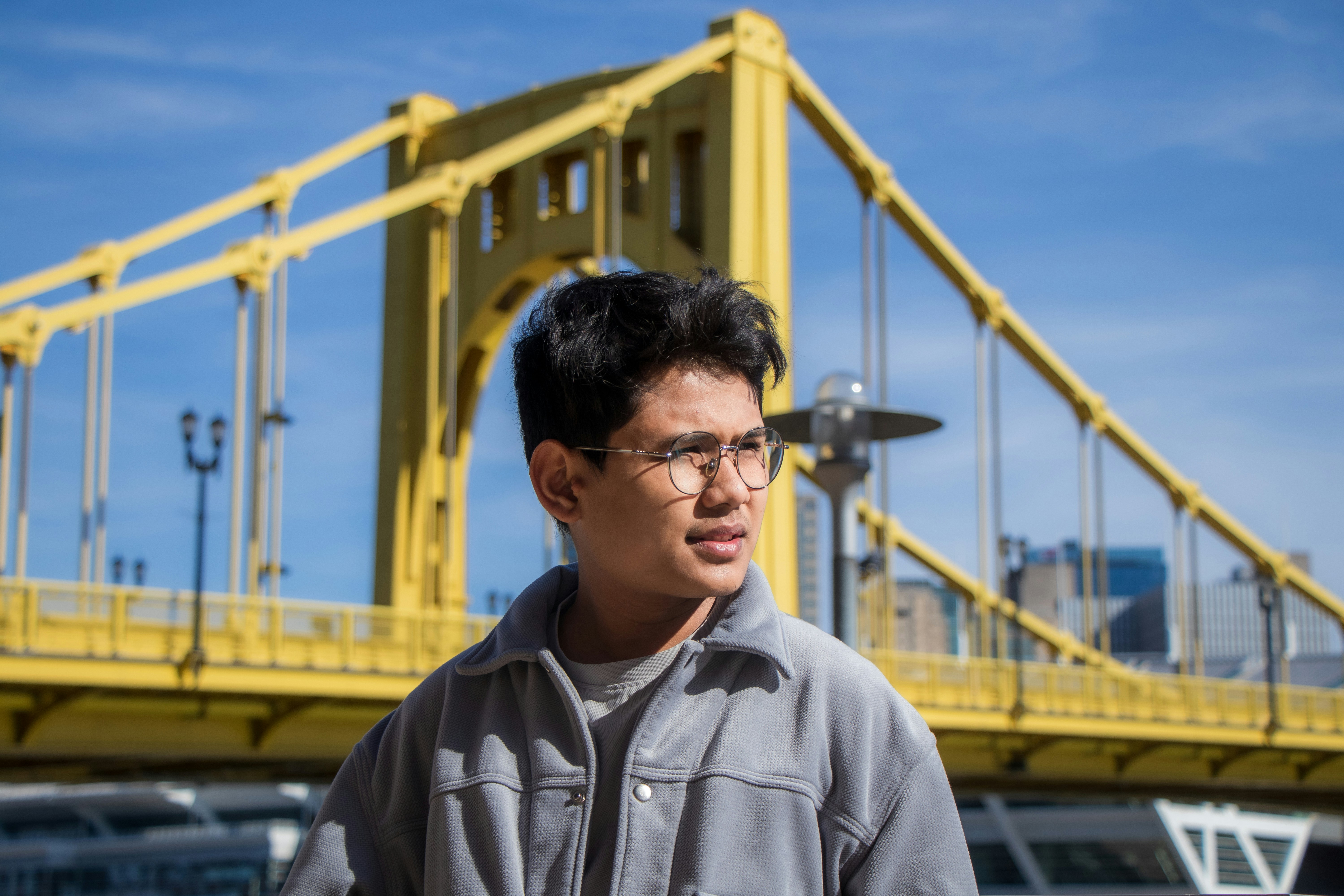 A man poses in front of a yellow bridge.