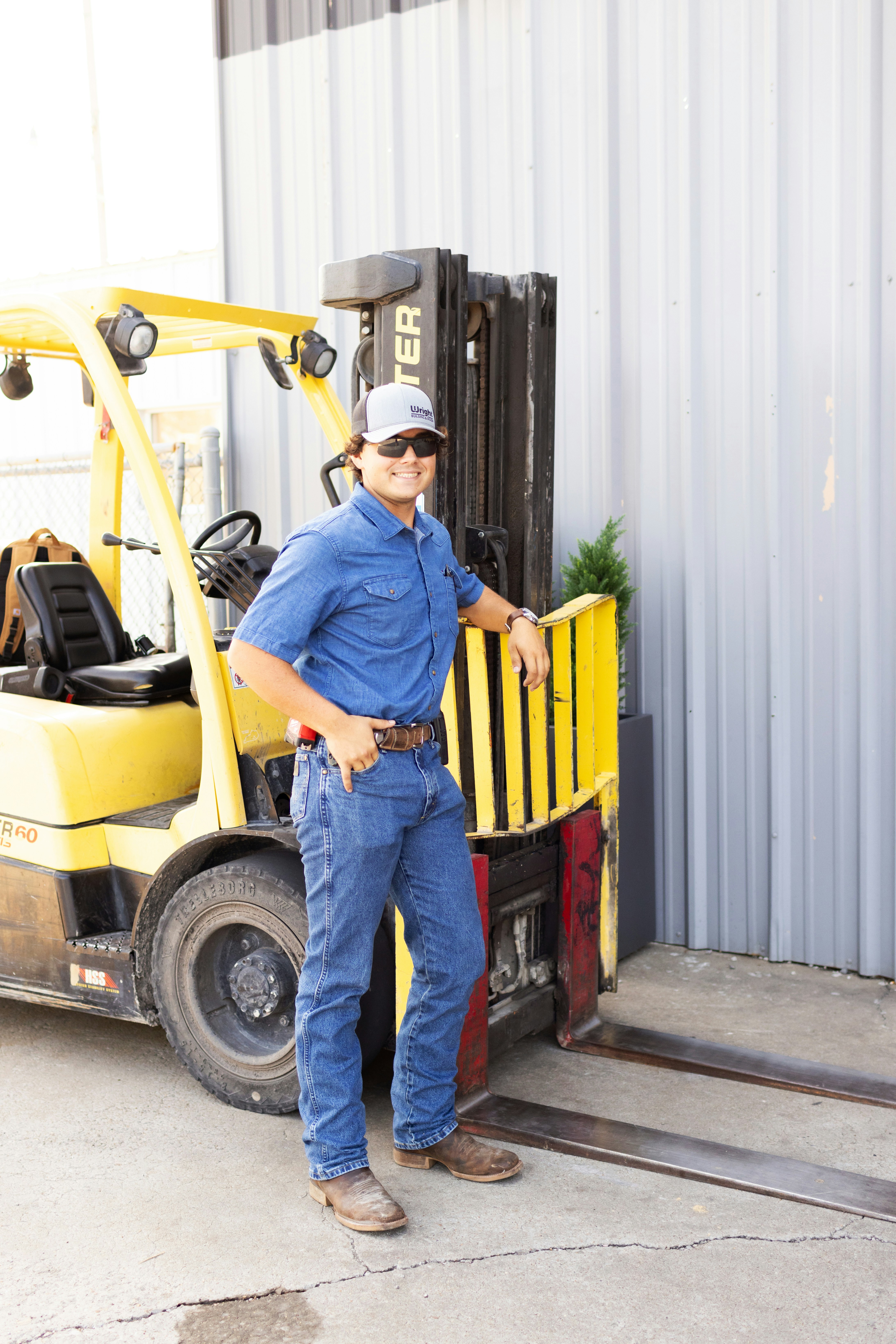 A man poses next to a forklift.