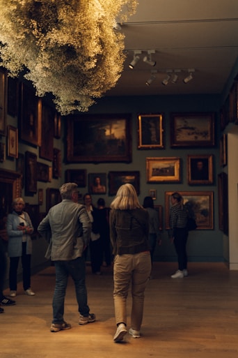 People view art in a gallery with floral installation.