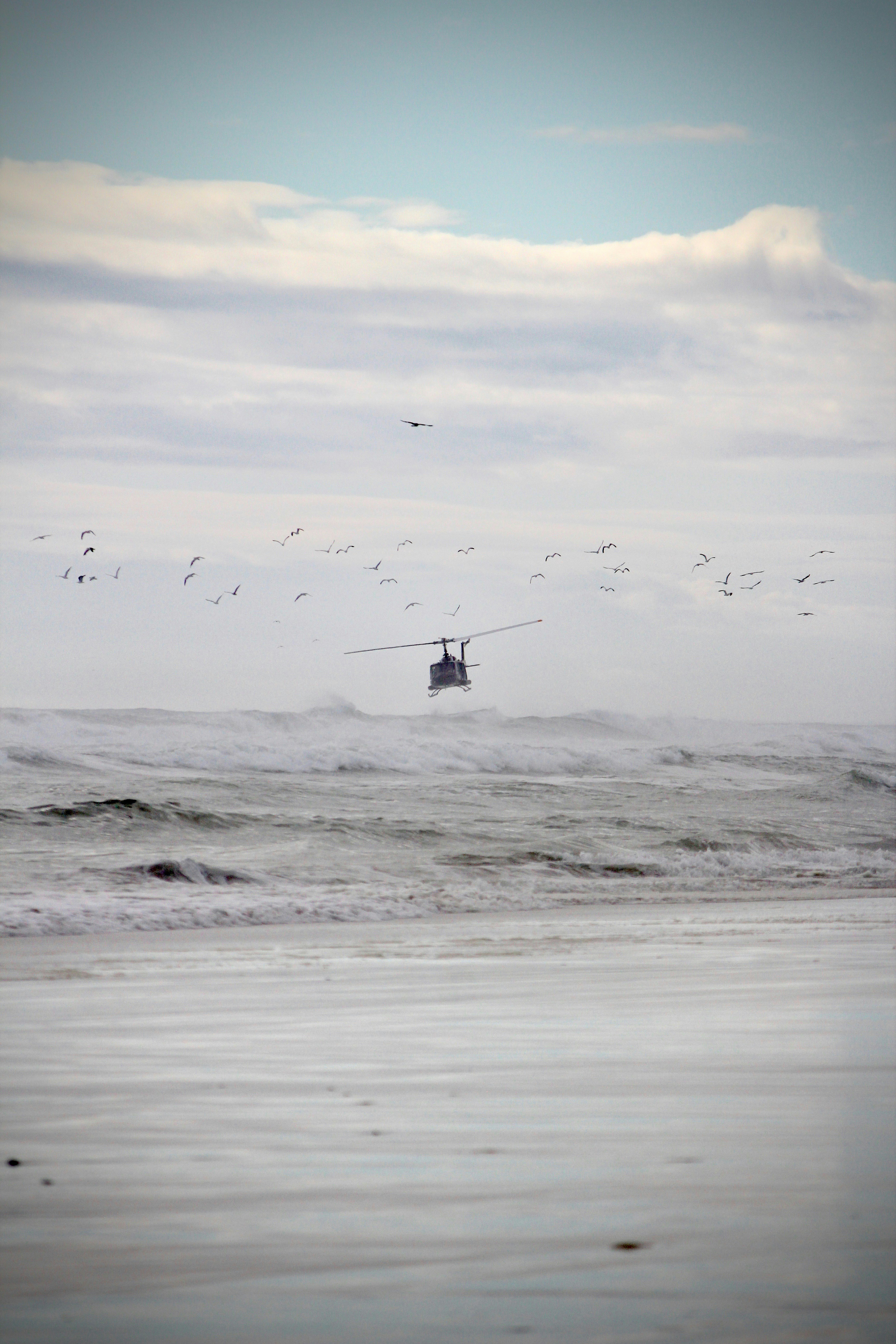 A helicopter flies over waves near the beach.