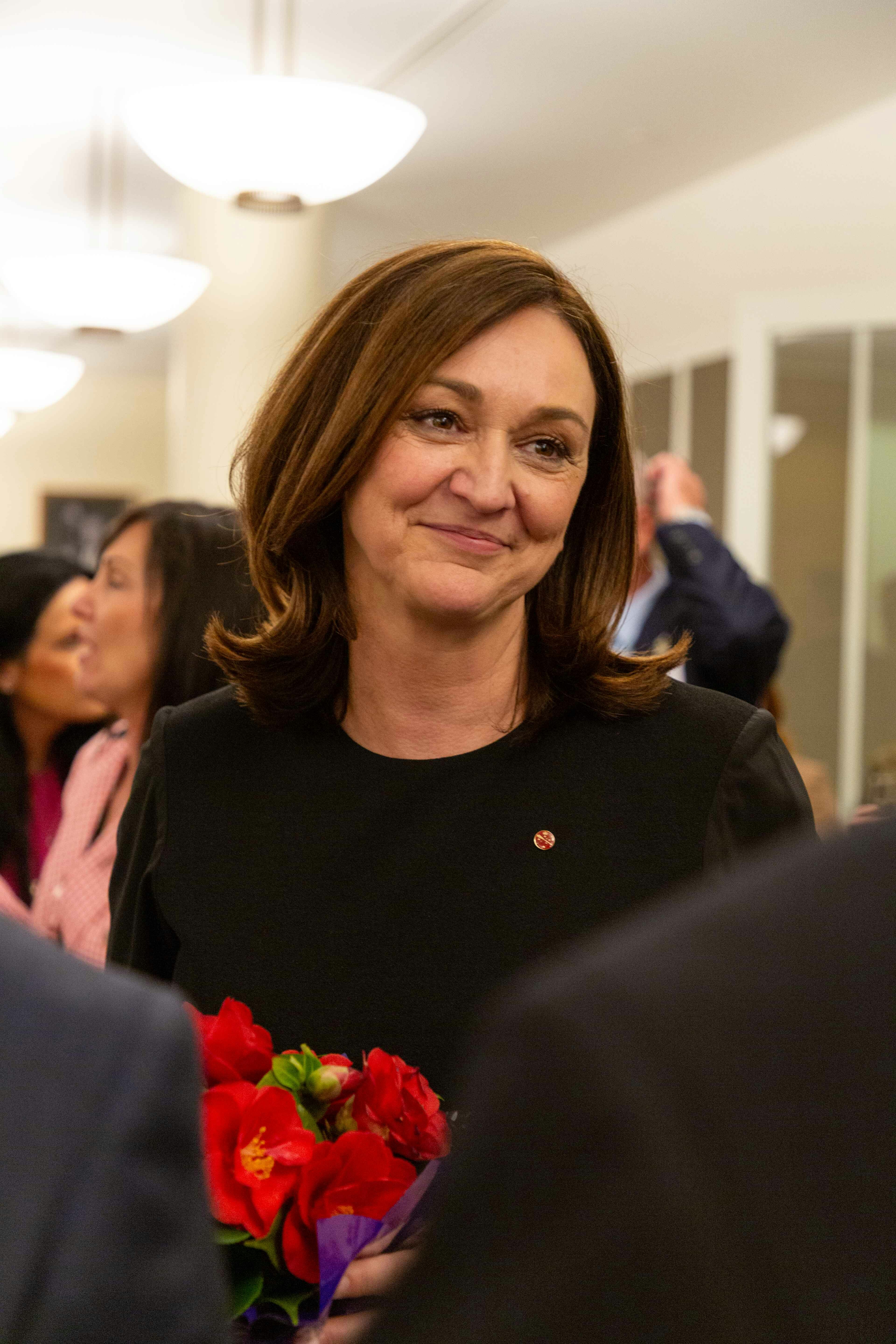 Woman smiles, holding flowers in a room.