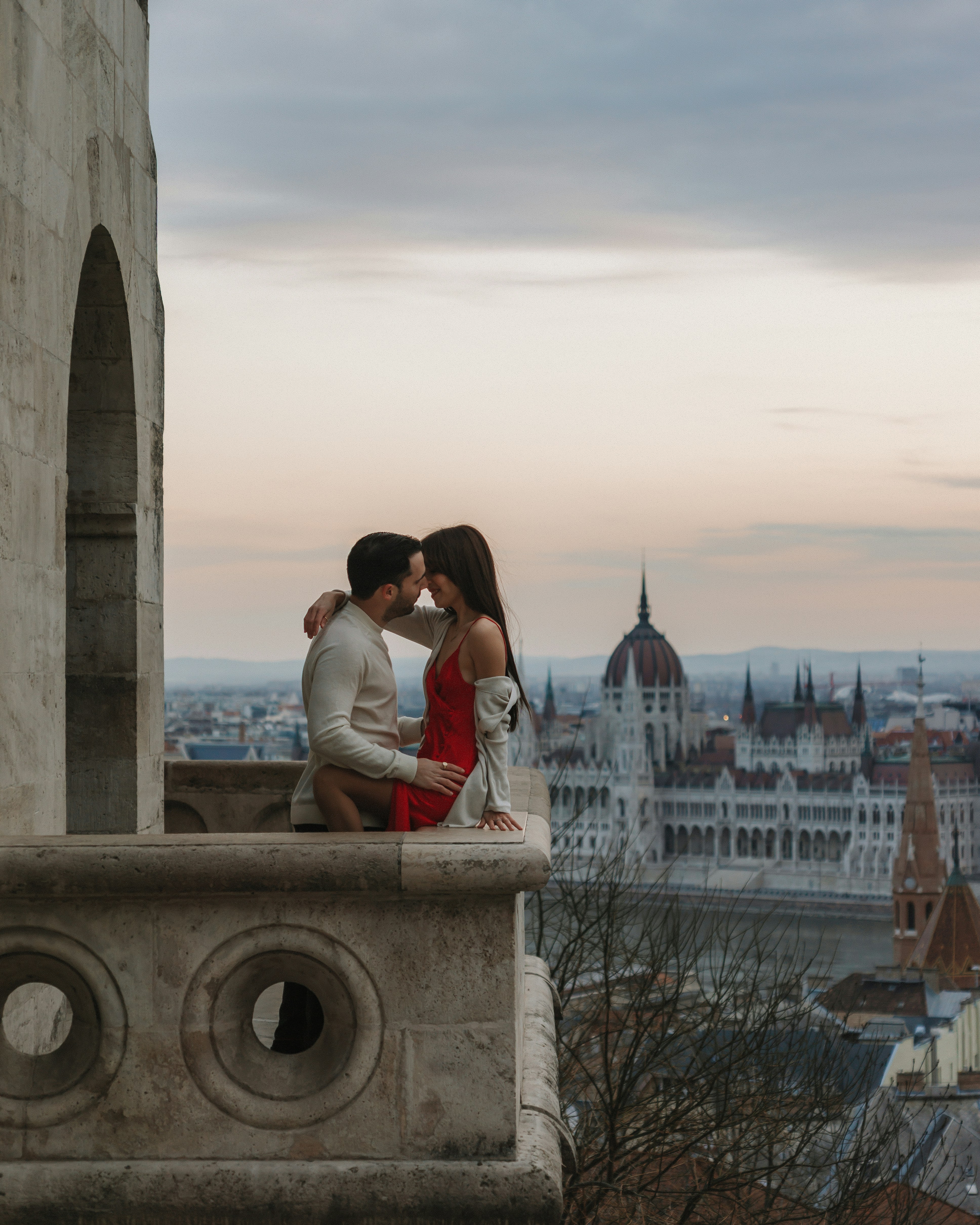 A couple embraces on a balcony overlooking the city.