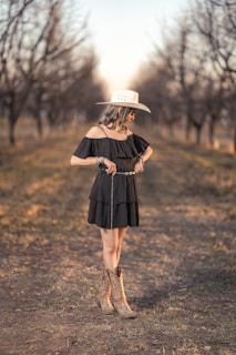Cowgirl poses in a field, wearing a dress and boots.