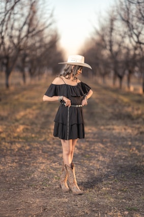 Cowgirl poses in a field, wearing a dress and boots.