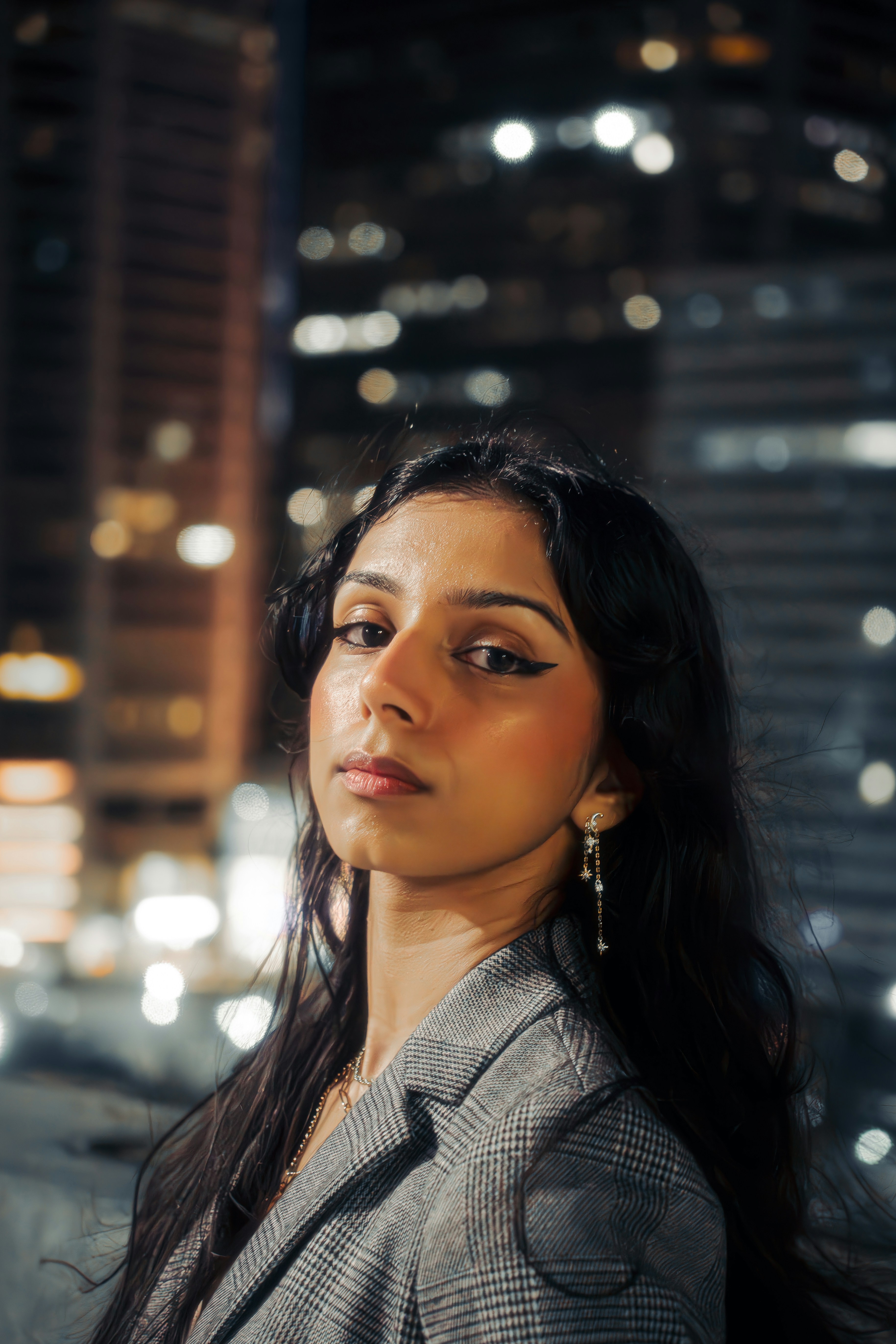 Woman poses with a city skyline backdrop at night.