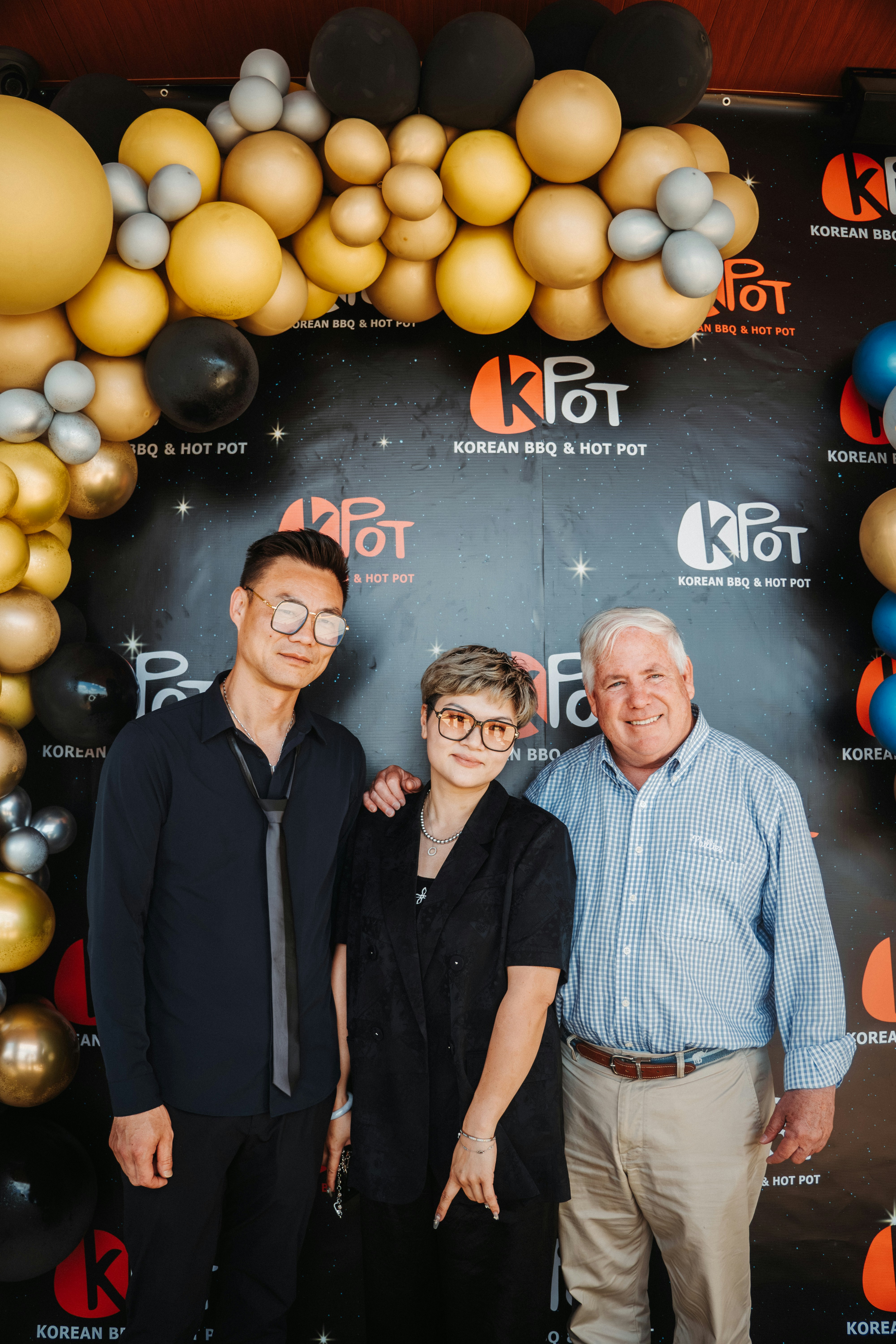 Three people pose in front of a korean restaurant backdrop.