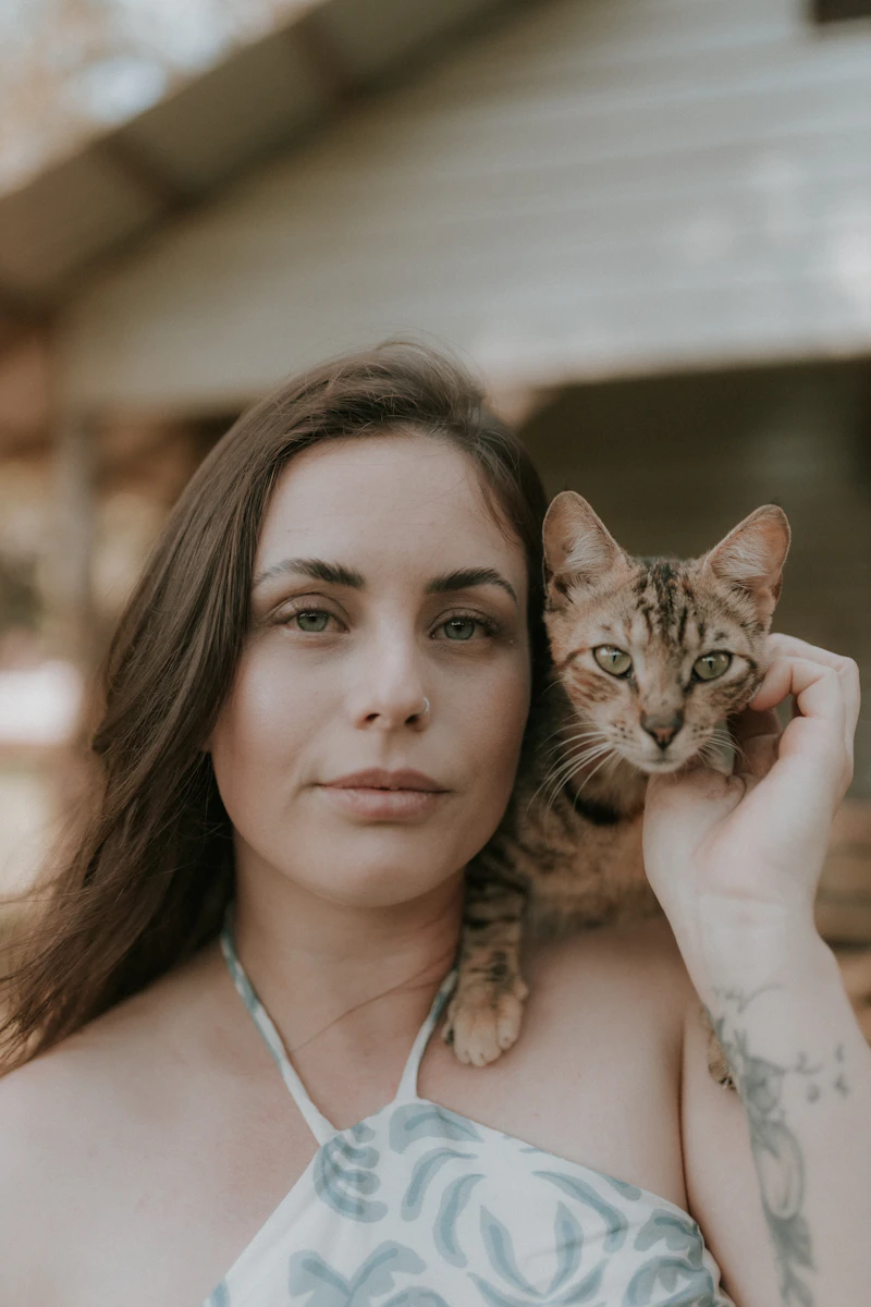 A woman holding a tabby cat against her shoulder