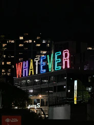Neon sign says "whatever" at night.