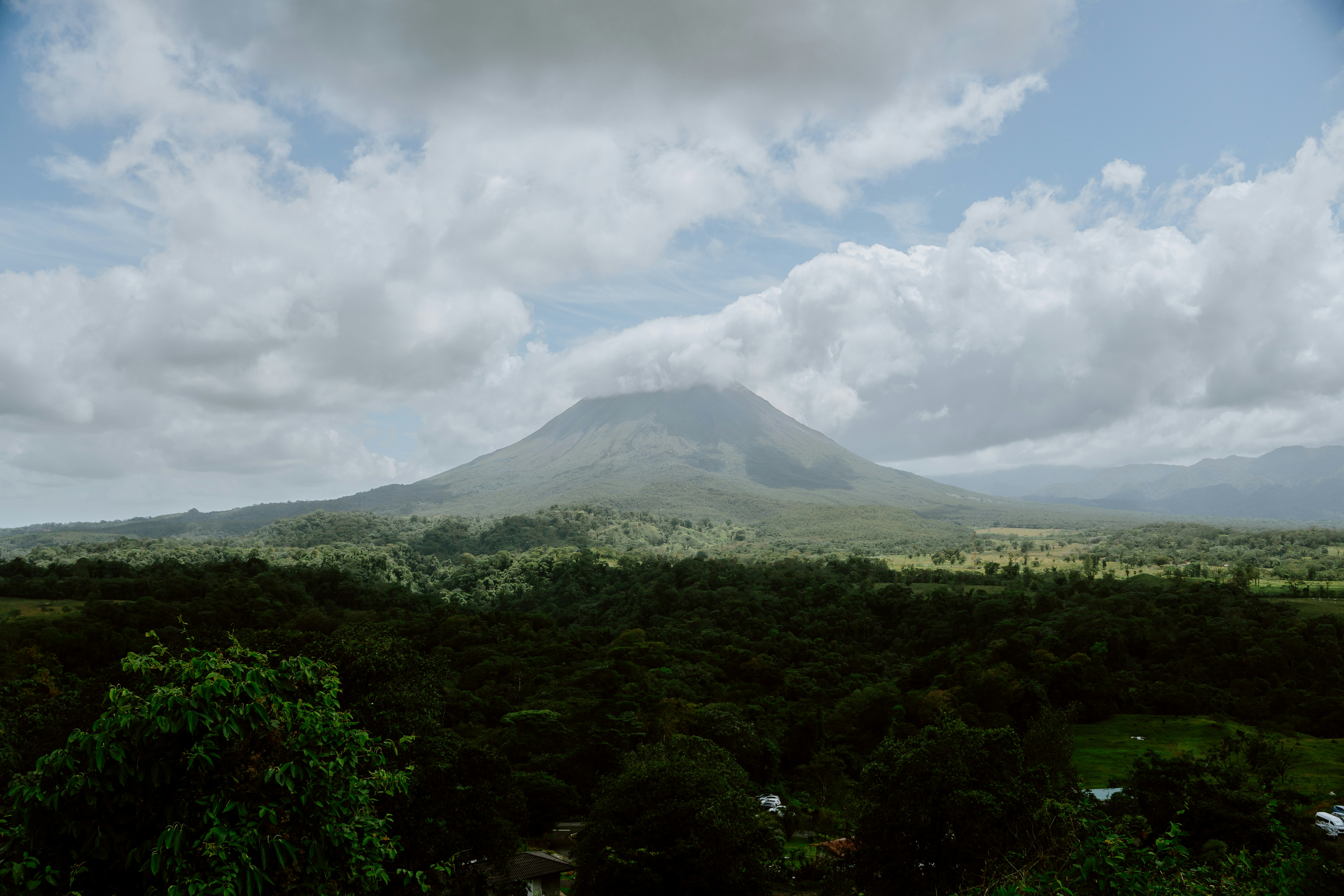A mountain stands tall amidst clouds and greenery., 