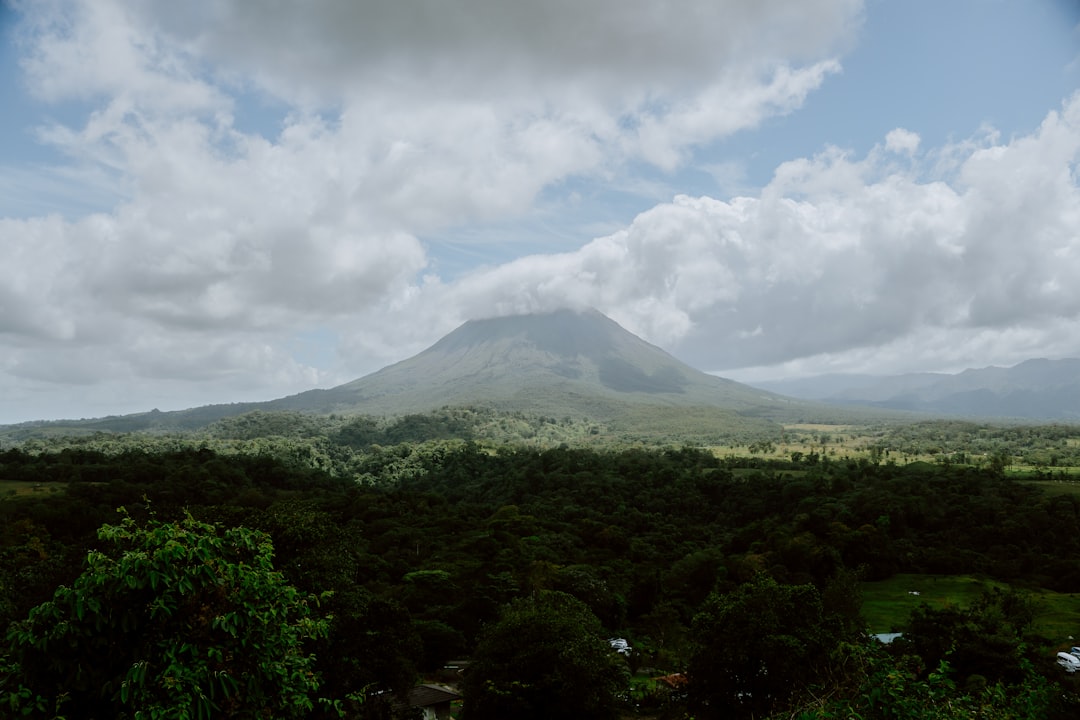 A mountain stands tall amidst clouds and greenery.,