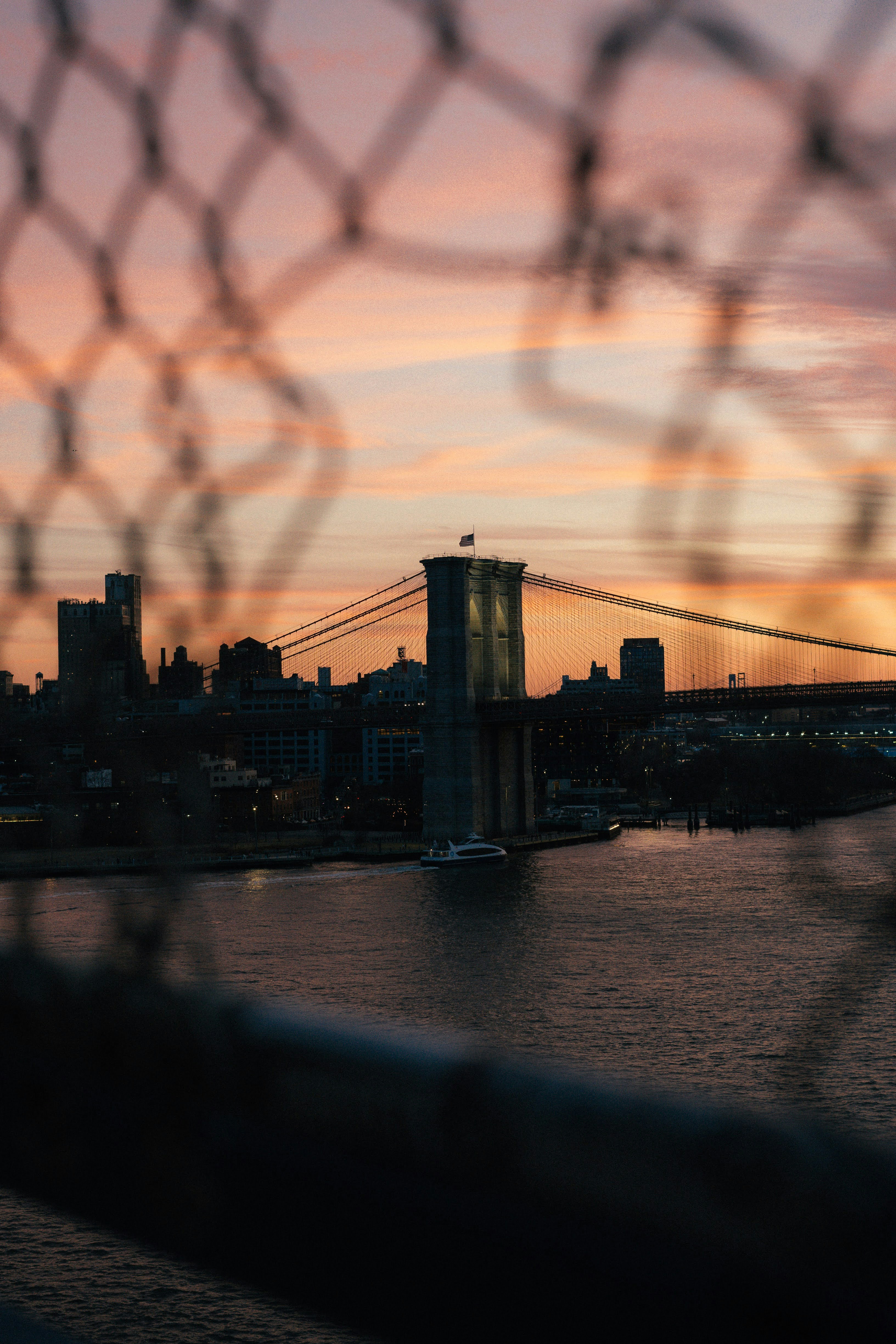 Brooklyn bridge at sunset, seen through a fence.
