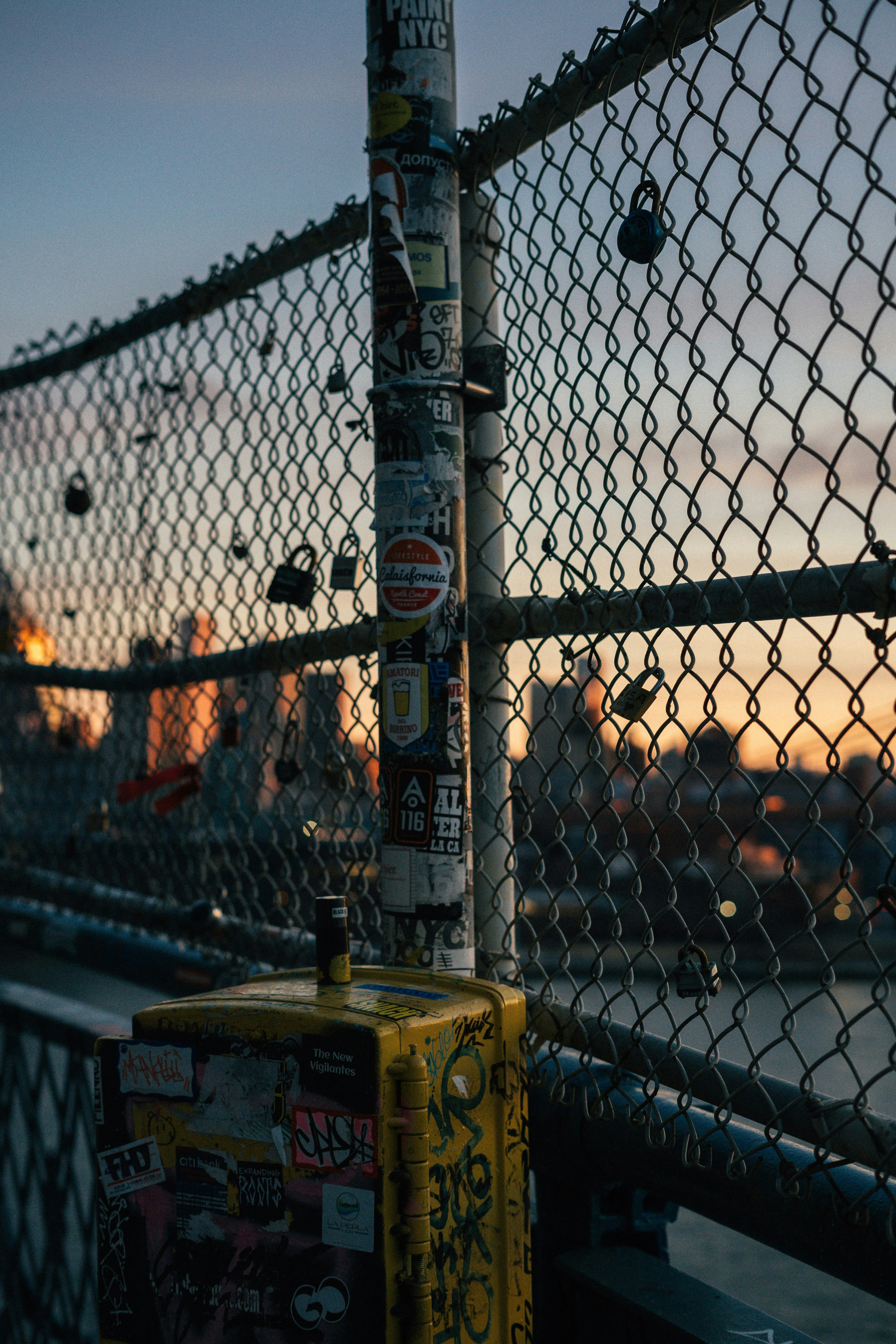 Locks and stickers decorate a fence against a sunset.