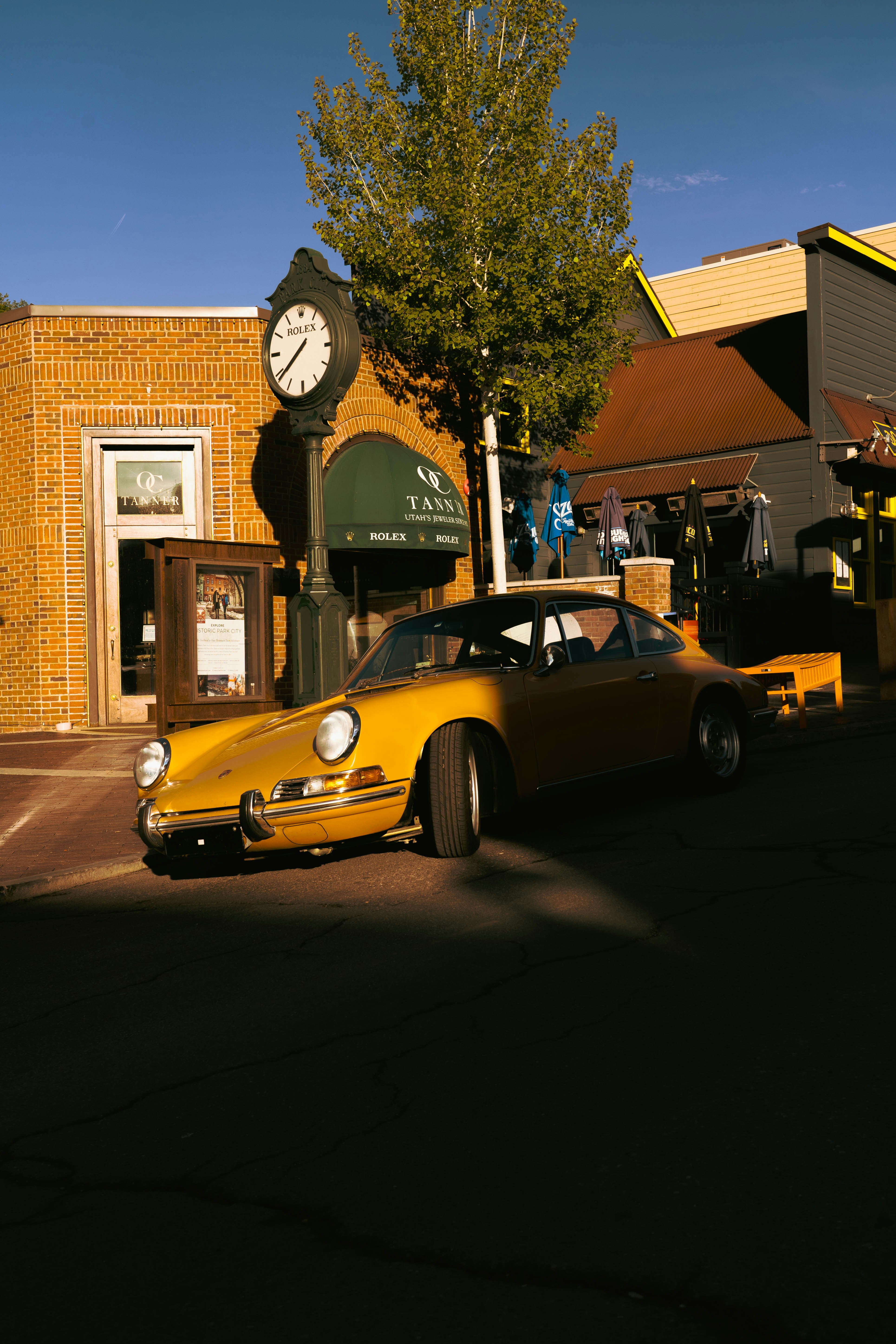 A yellow porsche parked by a clock tower.