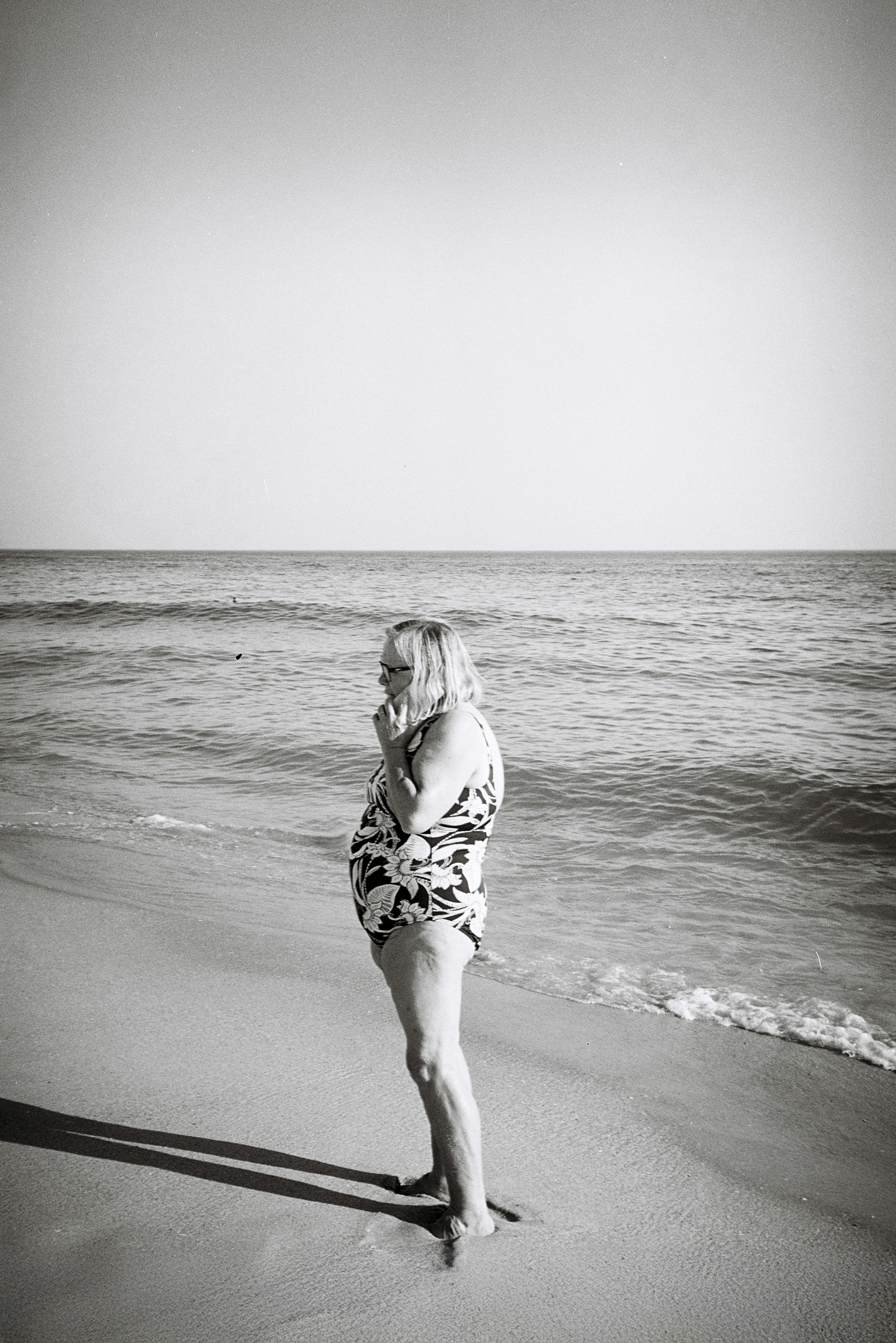 Woman in a swimsuit stands at the edge of the ocean.
