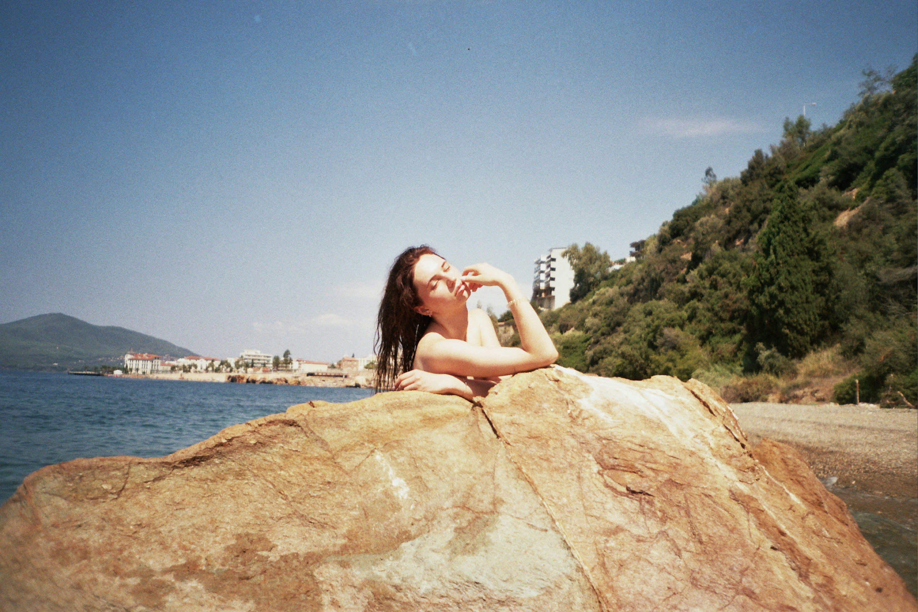 A woman poses on a rock near the ocean.