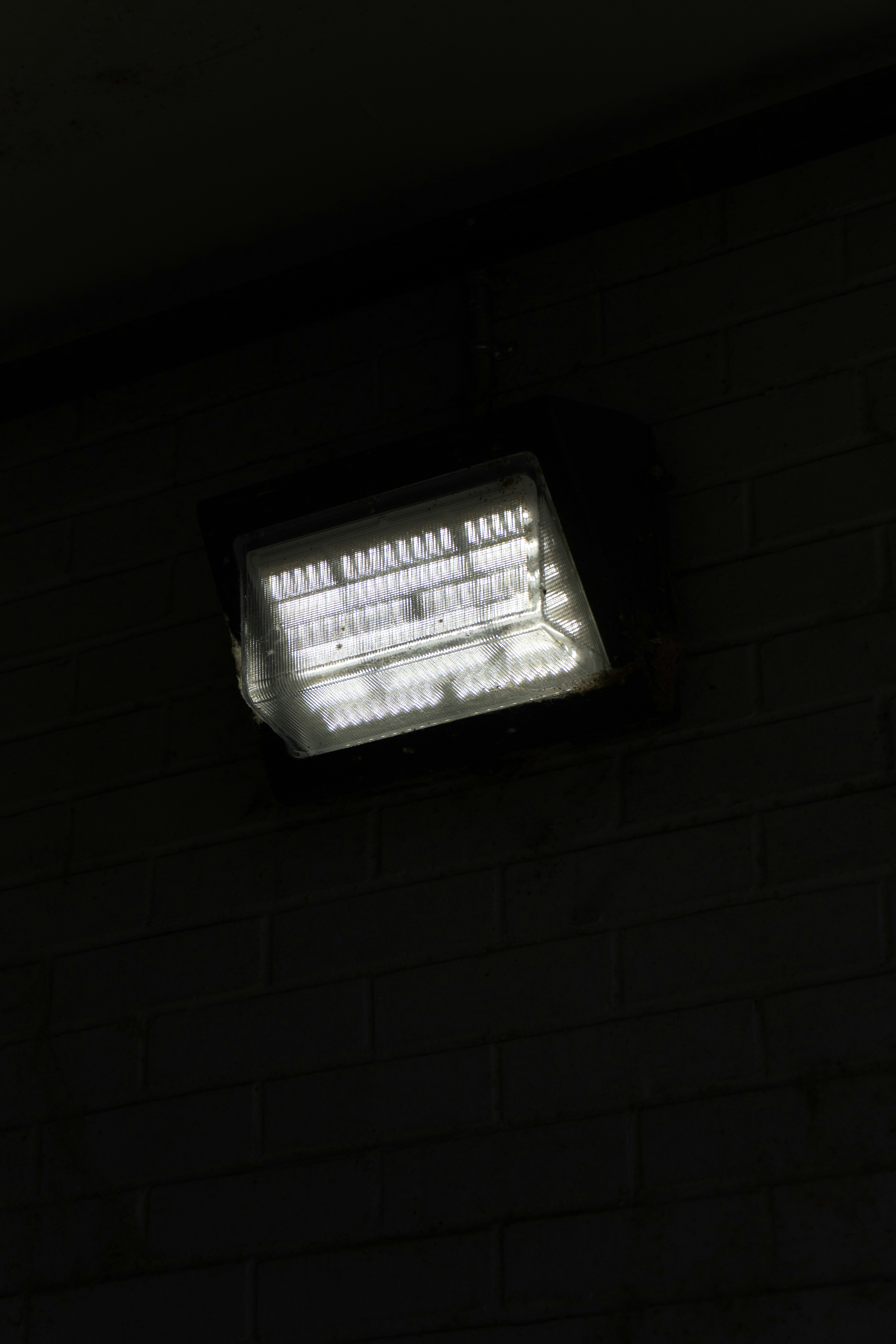 A bright light illuminates a dark brick wall.
