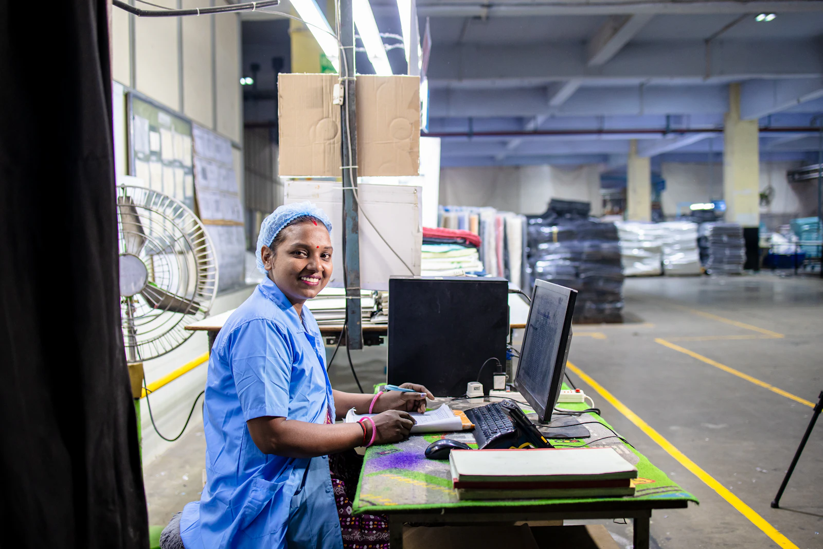 An Indian operator in a blue uniform entering data on the factory floor