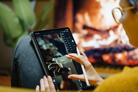 Someone is working on a tablet near a fireplace.