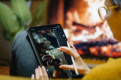 Someone is working on a tablet near a fireplace.