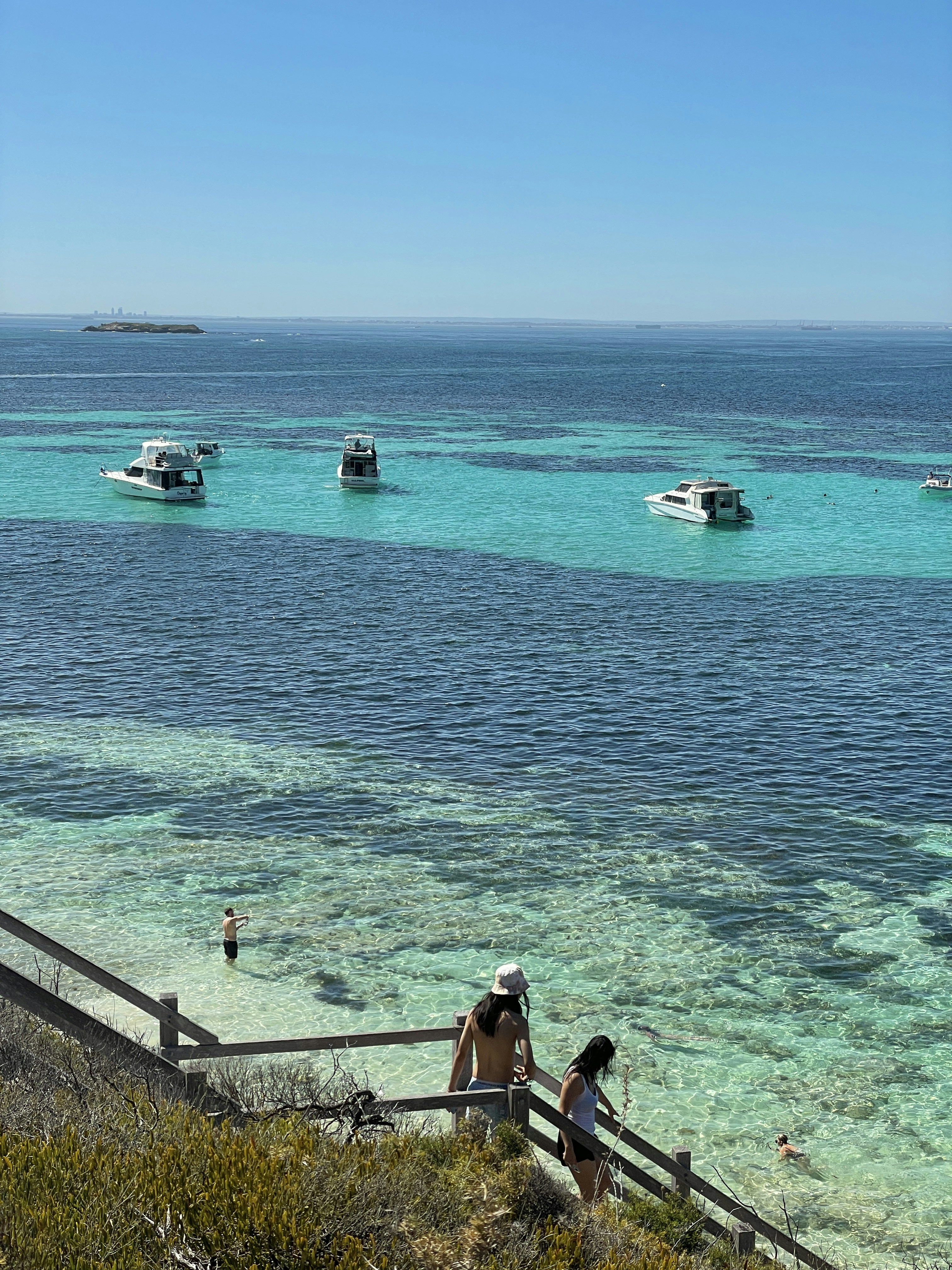 Boats float on turquoise waters, sunny day.