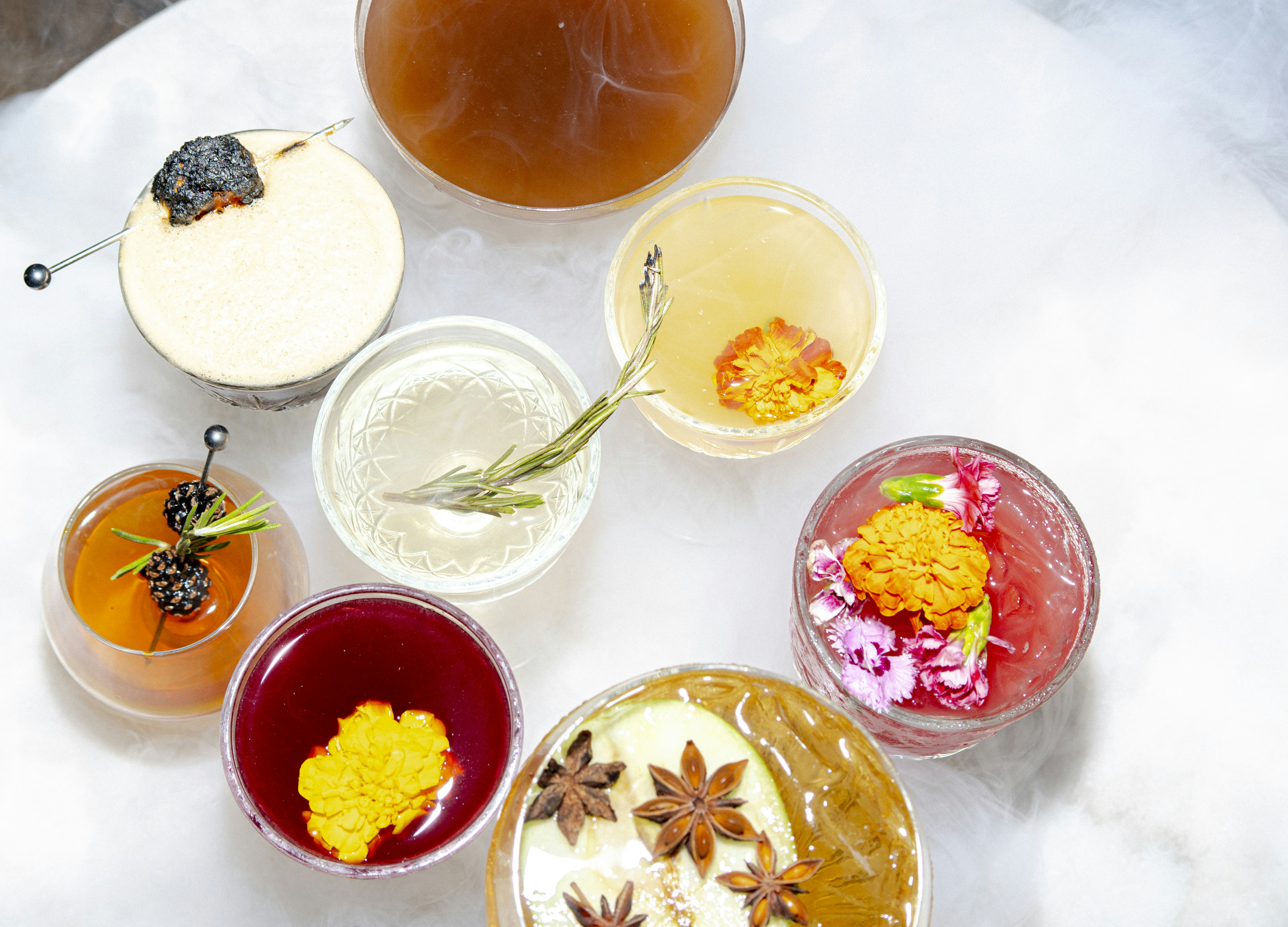 Various colorful cocktails beautifully garnished on a white surface.