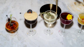 Five colorful cocktails are arranged on a surface
