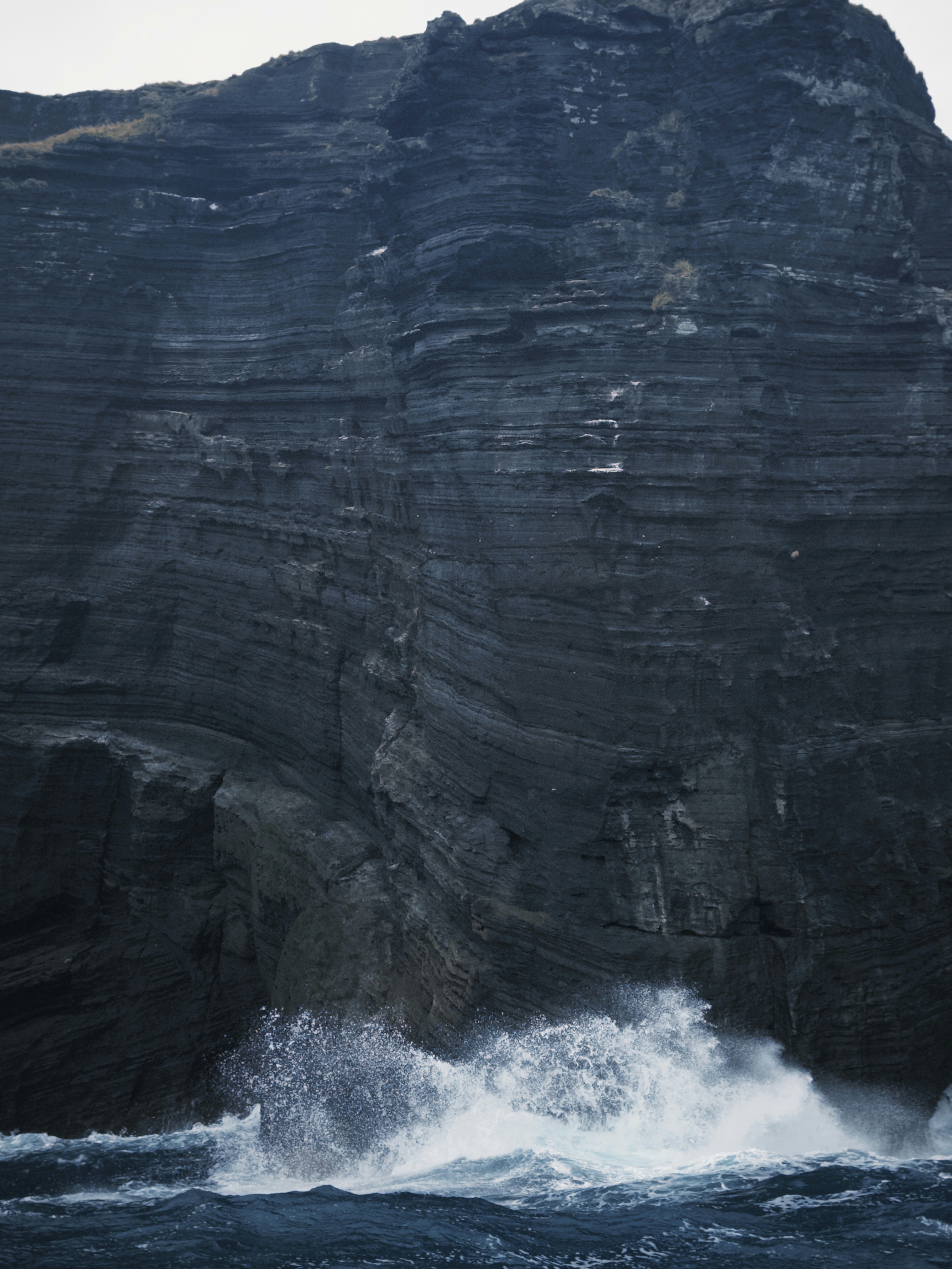 Waves crash against a dark, layered cliff.