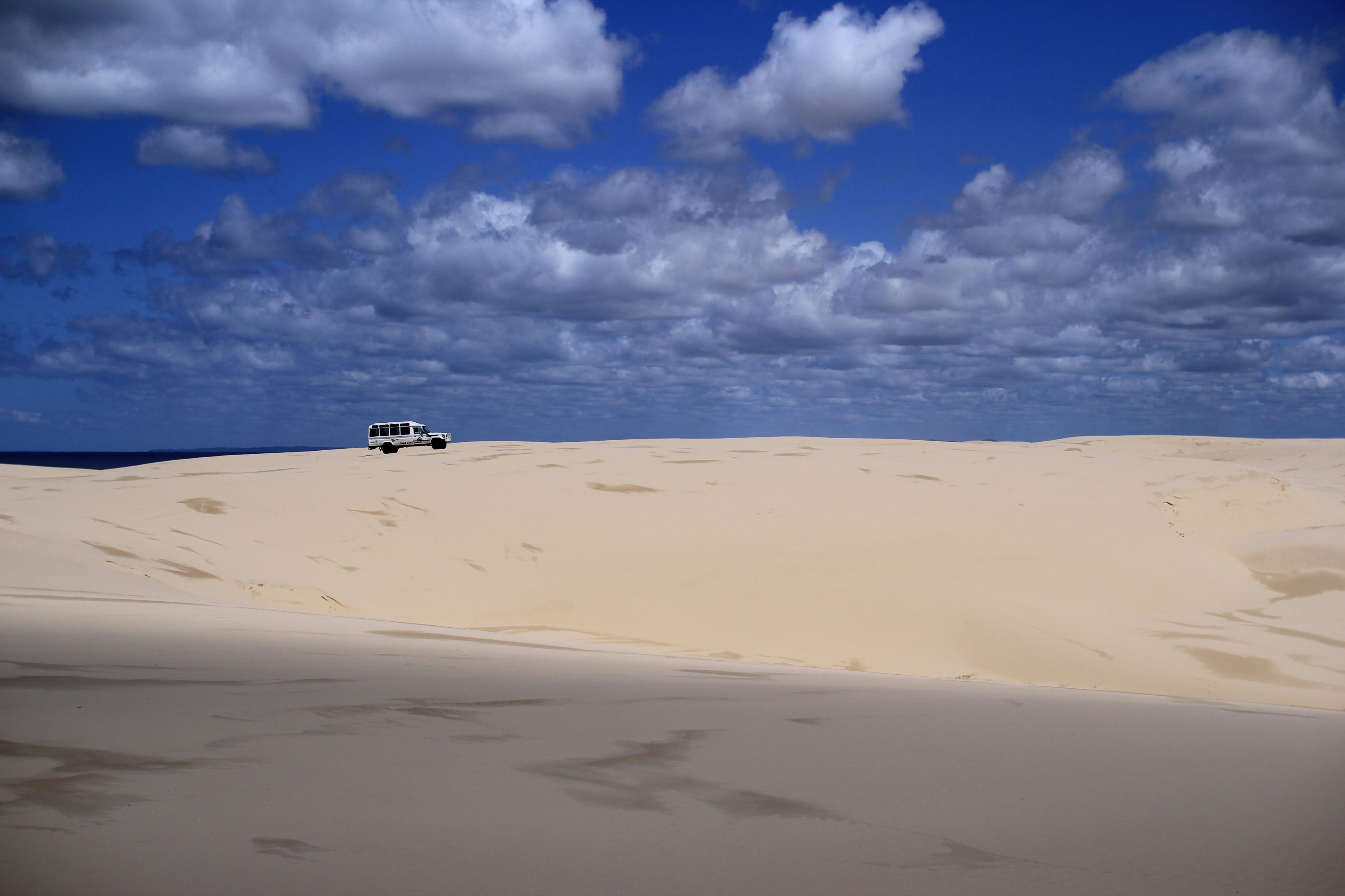 A car drives on sand dunes beneath a cloudy sky., 