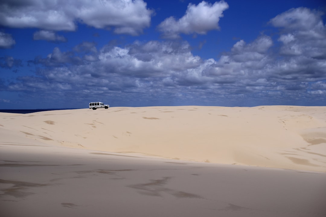 A car drives on sand dunes beneath a cloudy sky.,