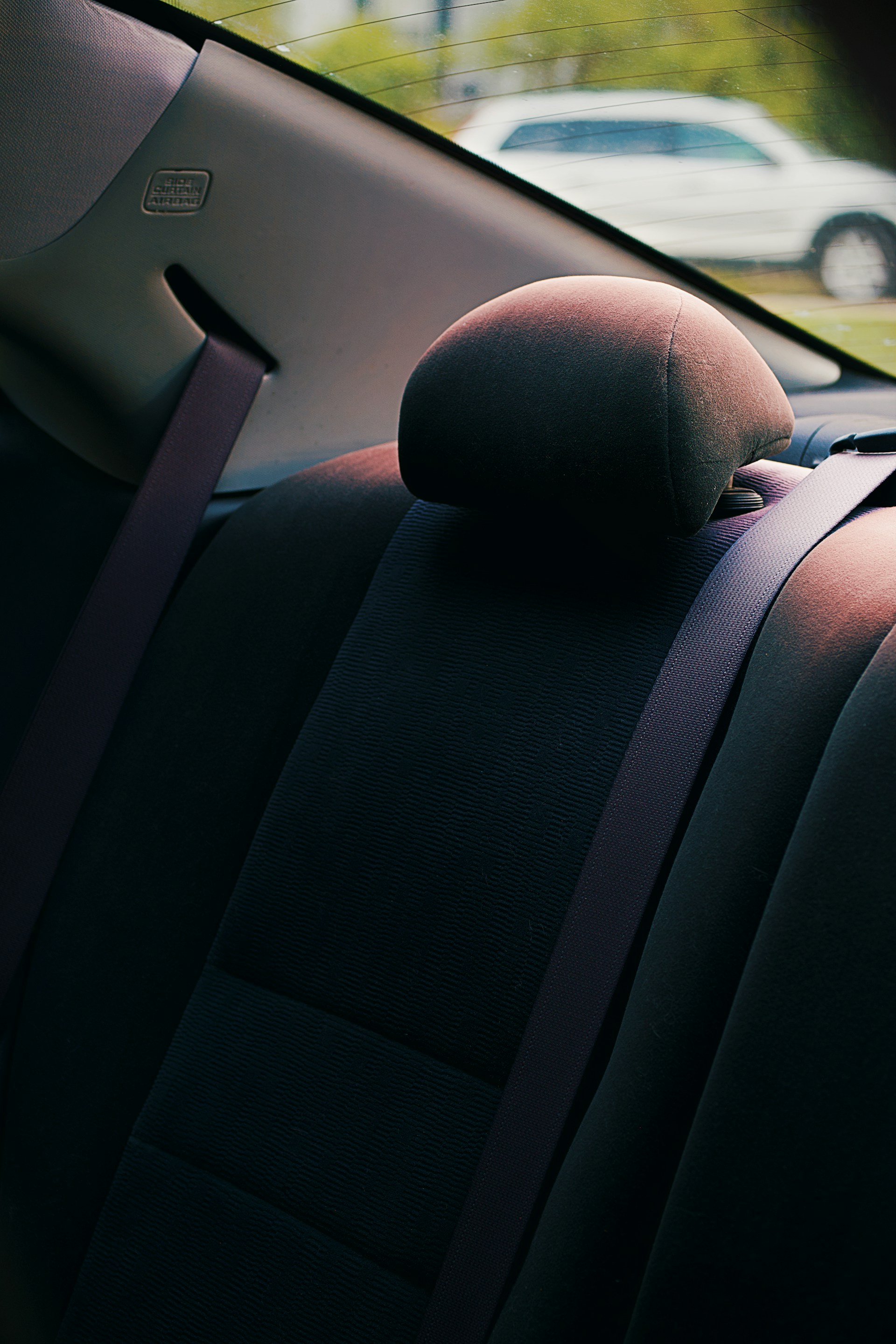 A dark back seat and headrest inside a car.