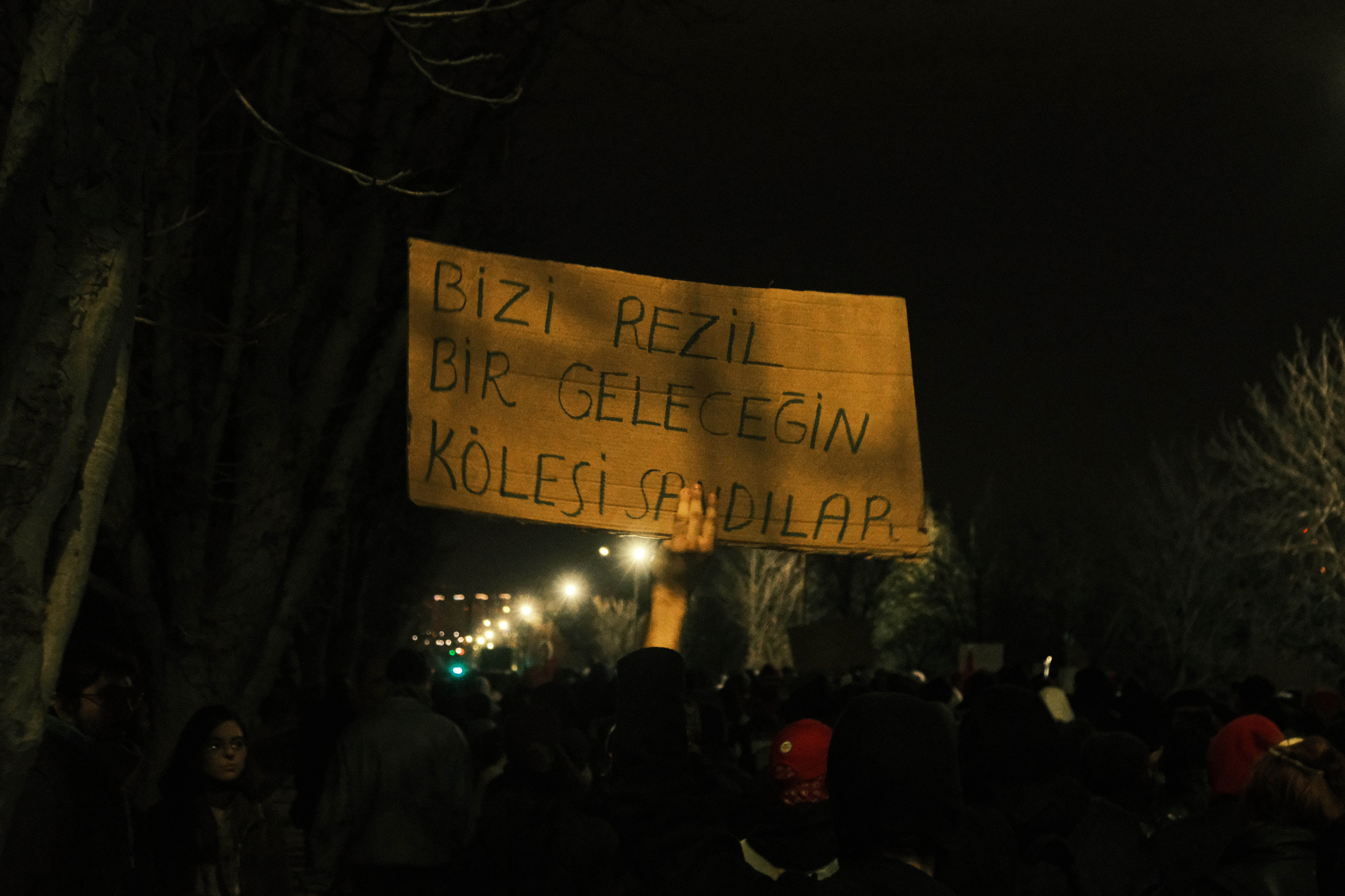 Protesters hold sign at night with a message.
