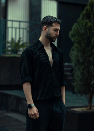 A man looks down, posing outdoors in black.