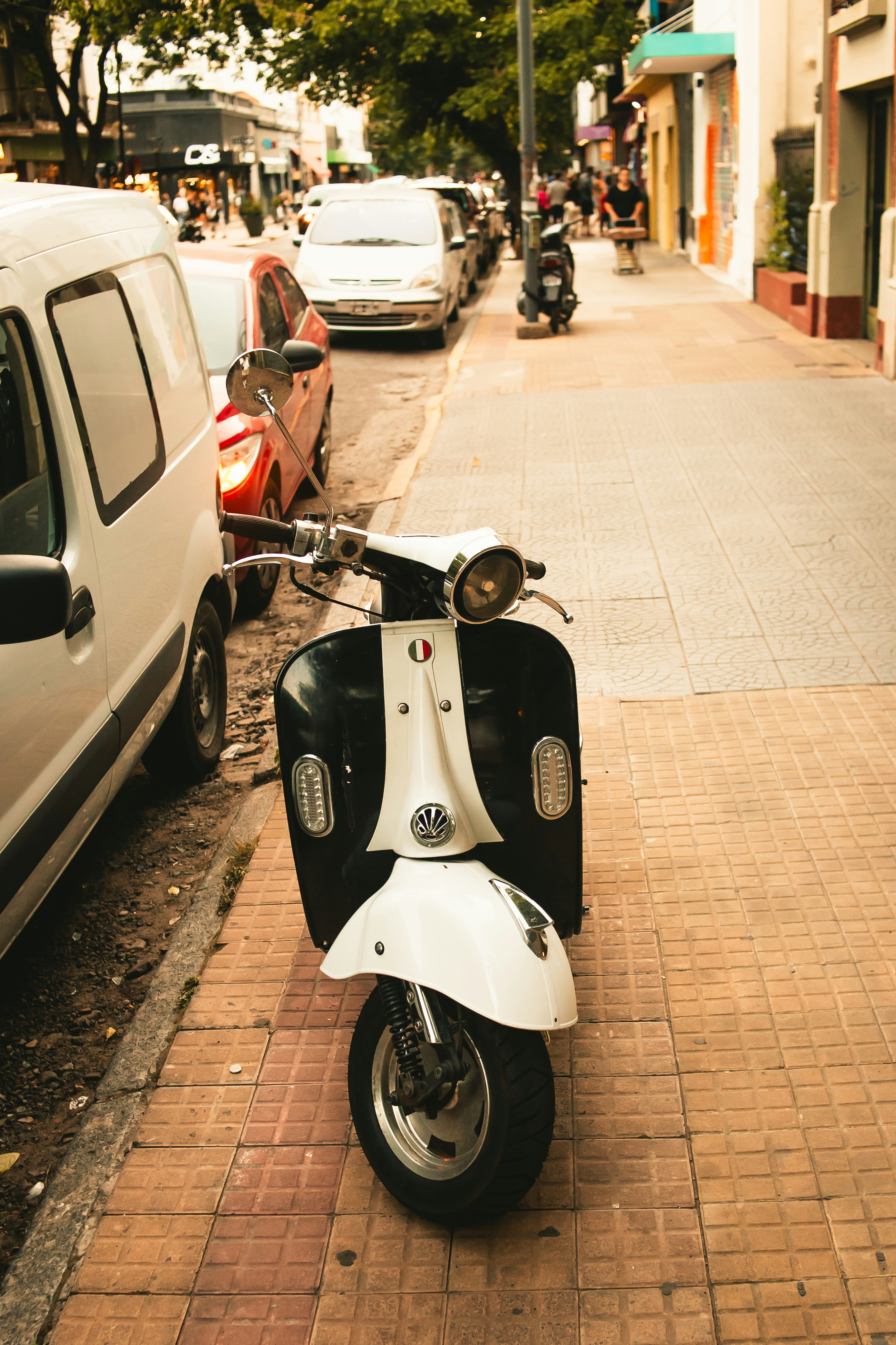 A retro scooter parks on the city sidewalk.