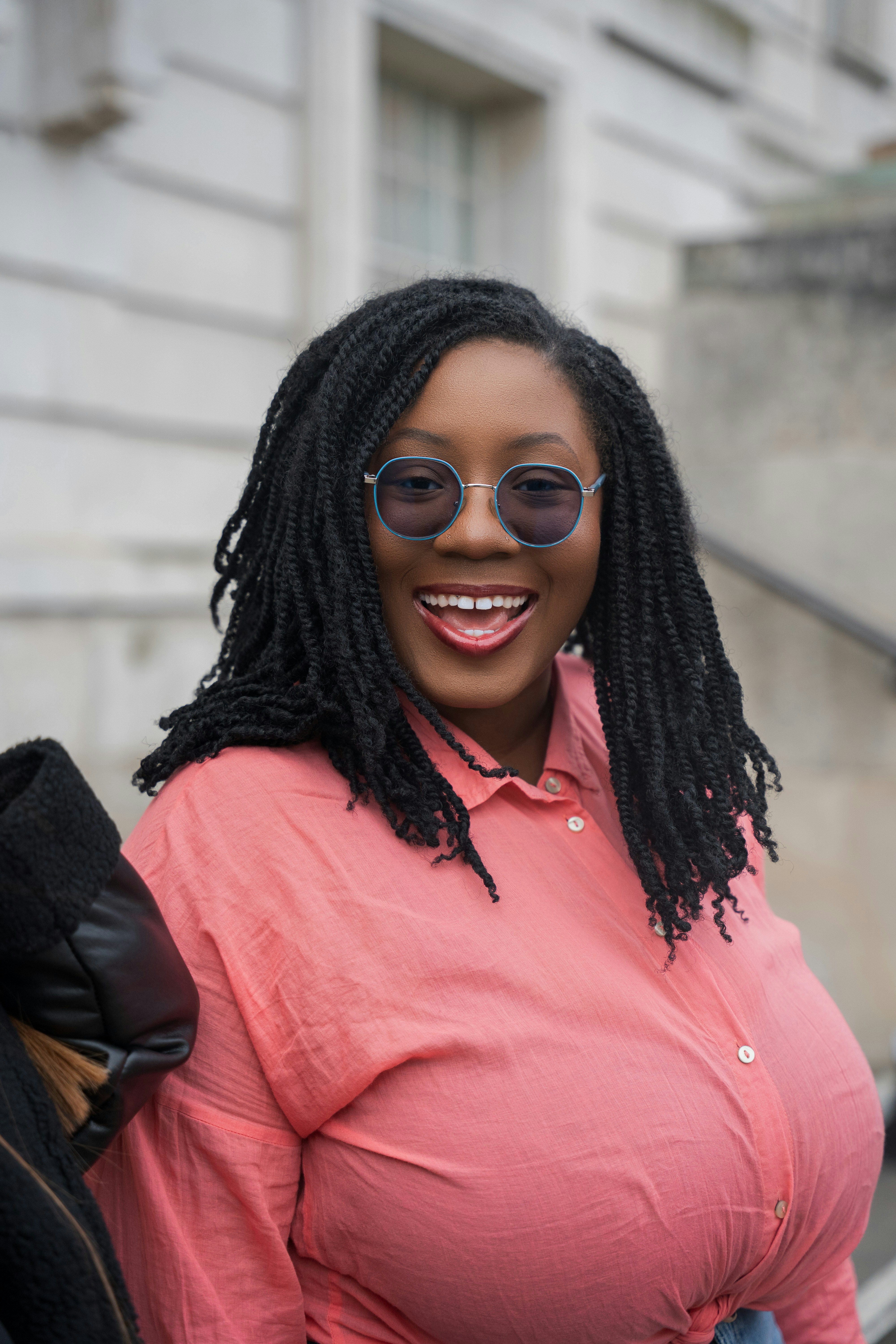 Woman with locs smiles wearing sunglasses.
