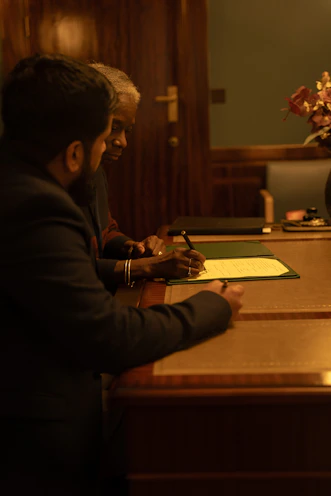Two people are signing a document at a desk.