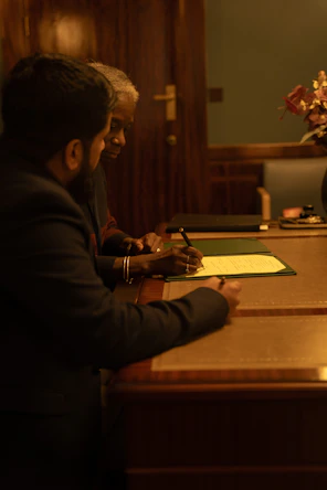 Two people are signing a document at a desk.