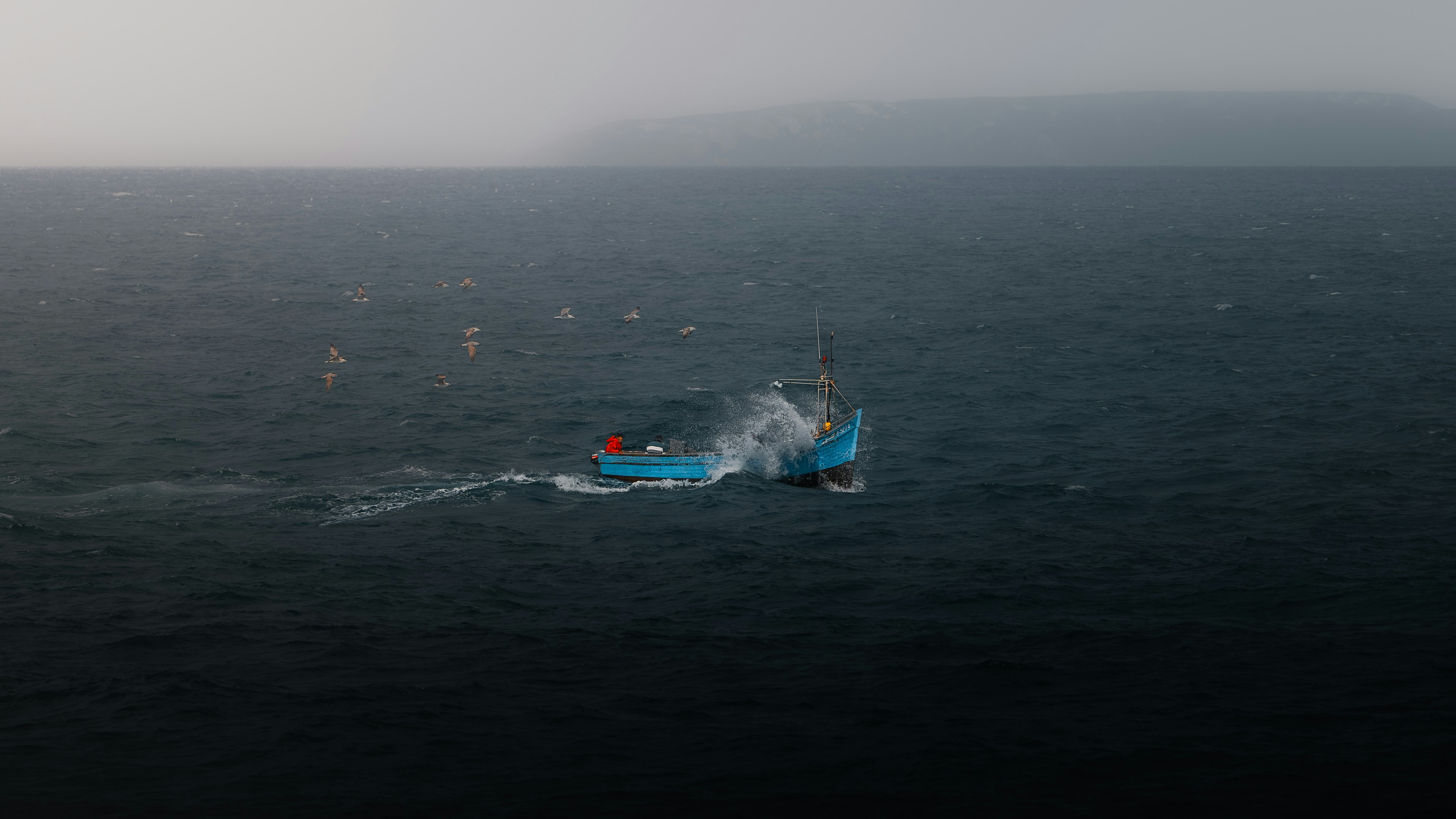 A blue boat sails across the dark sea.