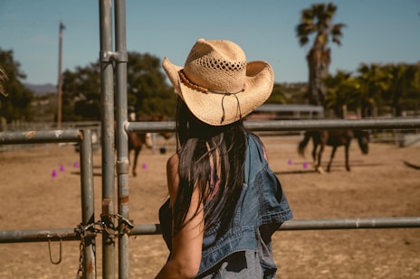 Cowgirl watches horses in a sunny corral.