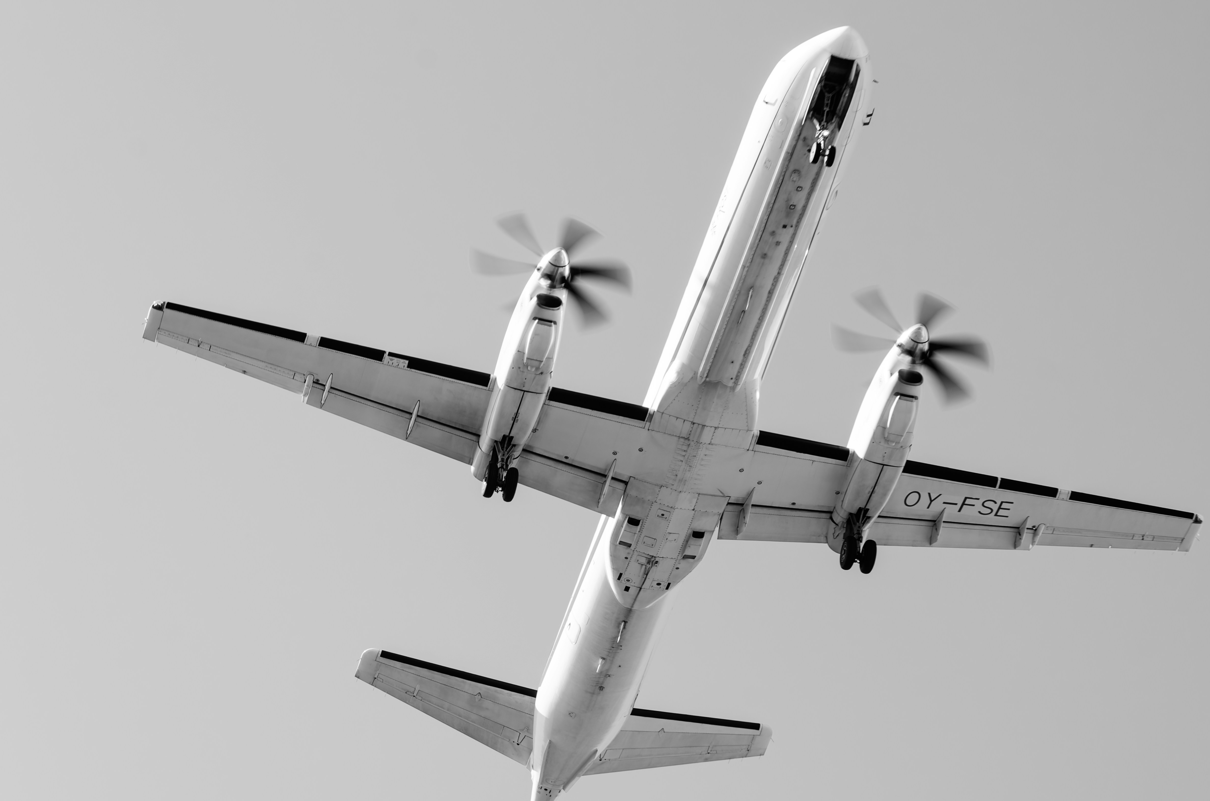 An airplane is flying overhead in black and white., Saab 2000 landing at Zagreb Airport.