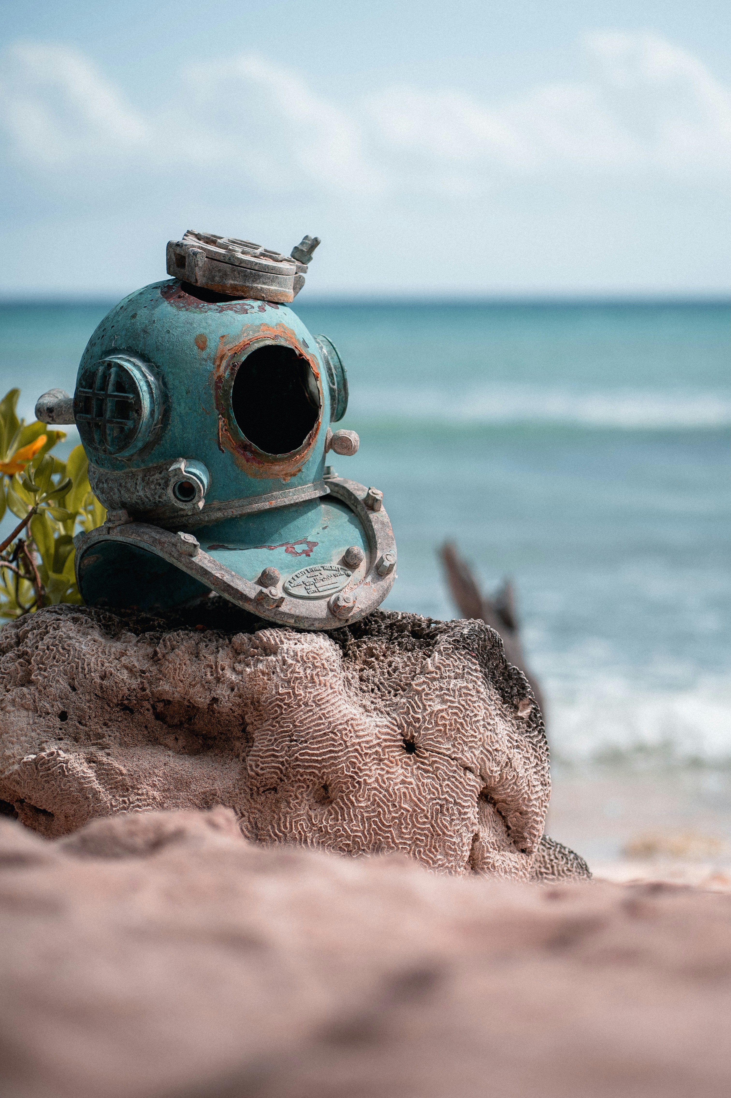 An old diving helmet rests on a rock by the sea.