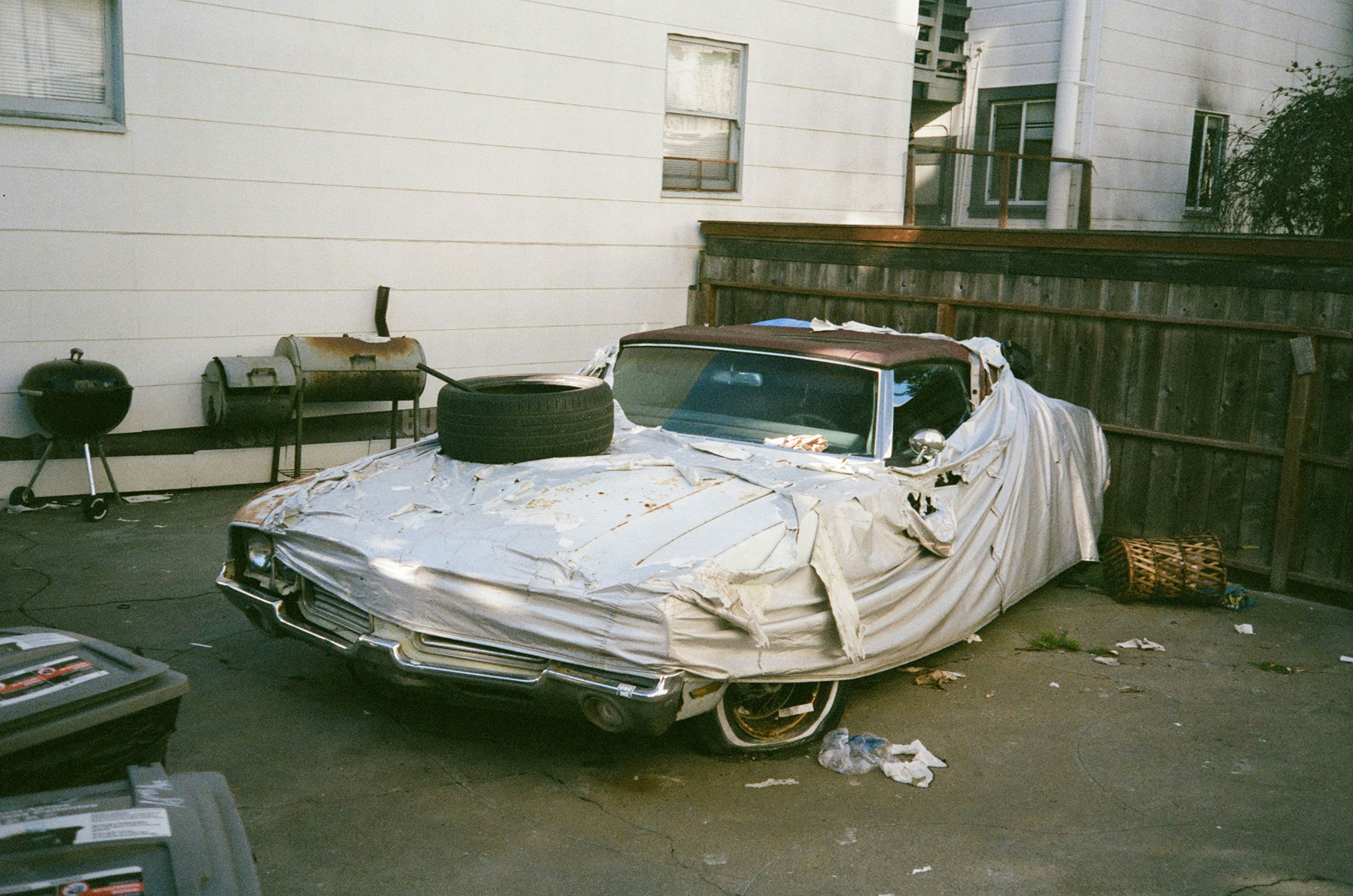 Old car under a sheet, stored in a backyard